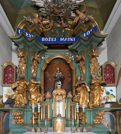 Zdjęcie nr 2: Tabernakulum w formie sześcianu, z wypukłym frontem. Drzwiczki w formie stojącego prostokąta zamkniętego łukiem półkolistym z aplikacją przedstawiającą kielich z hostią z monogramem IHS w glorii. Tron wystawienia architektoniczny, trójosiowy. Oś środkowa w postaci obrotowej niszy ujętej w profilowaną ramę, z konchą utworzoną z rocaille'u, zakończona ornamentalnym zwieńczeniem dekorowanym muszlą, małżowiną i kartuszem, które tworzą postument dla rzeźby baranka z krzyżem. Osie boczne na cokole, cofniętym pod kątem w tył, ujęte dwiema parami kolumn różnej wysokości o kapitelach kompozytowych, dźwigających pełne belkowanie w formie spływu, wyłamane w ich partii, na których znajdują się siedzące i klęczące figury aniołów. Między kolumnami prostokątne płyciny z wotami. Struktura polichromowana w kolorze jasnozielonym z pozłoconymi profilami i ornamentyką.