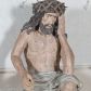 Zdjęcie nr 1: Figura pełnoplastyczna przedstawiająca Chrystusa Frasobliwego. Chrystus ukazany w pozycji siedzącej na kamiennej ławie, wspierający lewą ręką głowę, a prawą opierający na prawym kolanie, której dłoń ułożona jest do trzymania niezachowanego atrybutu. Ciało o silnie podkreślonej muskularnej i krępej budowie. Twarz podłużna, z długim i wąskim nosem, oczami skierowanymi w dół, okolona gęstą i kręconą brodą. Włosy długie, ciemnobrązowe, skręcone w pojedyncze pukle opadają na ramiona i plecy. Na głowie Chrystus ma założoną szeroką koronę cierniową, złożoną z przeplatających się symetrycznie gałązek z wystającymi cierniami. Perizonium białe, ciasno oplatające biodra, silnie drapowane. Polichromia w odsłoniętych partiach ciała naturalistyczna. Spod korony cierniowej oraz po całym ciele spływają drobne strużki krwi.

