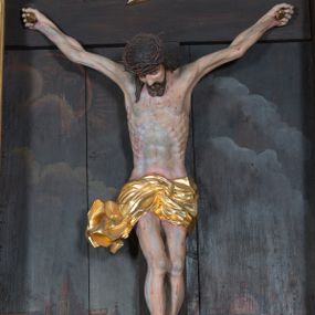 Zdjęcie nr 1: Krucyfiks umieszczony w polu środkowym ołtarza na tle malowanego pejzażu Jerozolimy, u dołu płaskorzeźbiona i złocona skała. Figura Chrystusa pełnoplastyczna ścięta w partii bioder, przybita do drewnianego krzyża trzema gwoździami. Sylwetka wychudzona z wyraźnie zaznaczoną muskulaturą i układem kostnym zwłaszcza w partii klatki piersiowej. Ramiona uniesione wysoko tworzą głęboki łuk. Ręce lekko zgięte, palce dłoni zaciśnięte. Głowa w koronie cierniowej opada na klatkę piersiową, nieznacznie przechylona w prawą stronę. Nogi lekko ugięte, stopy skrzyżowane, przybite jednym gwoździem. Twarz Chrystusa pociągła, okolona długimi włosami opadającymi na prawe ramię oraz krótką brodą. Oczy zamknięte, nos prosty, usta wąskie i rozchylone. Wokół bioder Chrystus ma zawieszone krótkie perizonium, bogato drapowane, z rozwianą kaskadą fałd przy prawym boku. Nad głową wisi titulus w formie banderoli z napisem „IN/RI”.Karnacja ciała w odcieniu szaro-różowym z zaznaczonymi śladami męki  na całym ciele. Włosy i zarost ciemnobrązowe, perizonium i gwoździe złocone, titulus złocony i srebrzony.

