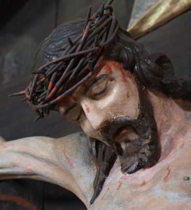 Zdjęcie nr 3: Krucyfiks umieszczony w polu środkowym ołtarza na tle malowanego pejzażu Jerozolimy, u dołu płaskorzeźbiona i złocona skała. Figura Chrystusa pełnoplastyczna ścięta w partii bioder, przybita do drewnianego krzyża trzema gwoździami. Sylwetka wychudzona z wyraźnie zaznaczoną muskulaturą i układem kostnym zwłaszcza w partii klatki piersiowej. Ramiona uniesione wysoko tworzą głęboki łuk. Ręce lekko zgięte, palce dłoni zaciśnięte. Głowa w koronie cierniowej opada na klatkę piersiową, nieznacznie przechylona w prawą stronę. Nogi lekko ugięte, stopy skrzyżowane, przybite jednym gwoździem. Twarz Chrystusa pociągła, okolona długimi włosami opadającymi na prawe ramię oraz krótką brodą. Oczy zamknięte, nos prosty, usta wąskie i rozchylone. Wokół bioder Chrystus ma zawieszone krótkie perizonium, bogato drapowane, z rozwianą kaskadą fałd przy prawym boku. Nad głową wisi titulus w formie banderoli z napisem „IN/RI”.Karnacja ciała w odcieniu szaro-różowym z zaznaczonymi śladami męki  na całym ciele. Włosy i zarost ciemnobrązowe, perizonium i gwoździe złocone, titulus złocony i srebrzony.

