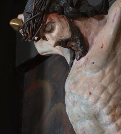 Zdjęcie nr 2: Krucyfiks umieszczony w polu środkowym ołtarza na tle malowanego pejzażu Jerozolimy, u dołu płaskorzeźbiona i złocona skała. Figura Chrystusa pełnoplastyczna ścięta w partii bioder, przybita do drewnianego krzyża trzema gwoździami. Sylwetka wychudzona z wyraźnie zaznaczoną muskulaturą i układem kostnym zwłaszcza w partii klatki piersiowej. Ramiona uniesione wysoko tworzą głęboki łuk. Ręce lekko zgięte, palce dłoni zaciśnięte. Głowa w koronie cierniowej opada na klatkę piersiową, nieznacznie przechylona w prawą stronę. Nogi lekko ugięte, stopy skrzyżowane, przybite jednym gwoździem. Twarz Chrystusa pociągła, okolona długimi włosami opadającymi na prawe ramię oraz krótką brodą. Oczy zamknięte, nos prosty, usta wąskie i rozchylone. Wokół bioder Chrystus ma zawieszone krótkie perizonium, bogato drapowane, z rozwianą kaskadą fałd przy prawym boku. Nad głową wisi titulus w formie banderoli z napisem „IN/RI”.Karnacja ciała w odcieniu szaro-różowym z zaznaczonymi śladami męki  na całym ciele. Włosy i zarost ciemnobrązowe, perizonium i gwoździe złocone, titulus złocony i srebrzony.

