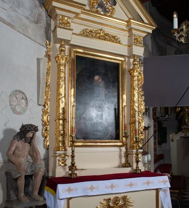 Zdjęcie nr 5: Ołtarz przyścienny, architektoniczny, jednoosiowy, jednokondygnacyjny. Ołtarz prostopadłościenny, skrzyniowy, mensa drewniana z kamiennym portatylem. Antepedium zdobione prostokątną płyciną o wklęsłych narożach, w której rzeźbiona uskrzydlona główka anielska. Retabulum ujęte parą kolumn, ustawionych na bazach. Trzony kolumn dekorowane w jednej trzeciej wysokości ornamentem okuciowym z rautami i kaboszonami, powyżej przewiązane opaską i zdobione w górnej części płaskorzeźbioną wicią winorośli. Powyżej kapiteli ustawione wazony wspierające wyłamane ponad nimi belkowanie z  trójkątnym, przerwanym przyczółkiem.  Pośrodku zwieńczenia pełnoplastyczna figura uskrzydlonego putta stojąca na kartuszu. Nastawa po bokach dekorowana ażurowymi, wąskimi uszakami formowanymi ze splotów z akantu i ornamentu rocaille'owego. Fryz zdobiony rzeźbioną wicią roślinną z rozetami. Pole środkowe w formie prostokątnej wnęki ujętej profilowaną ramą; wewnątrz obraz z przedstawieniem św. Idziego. Całość struktury ołtarza polichromowana w odcieniu jasnego beżu, detal architektoniczny, ornamentyka i profilowania złocone; pole kartusza i szata aniołka srebrzone.