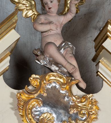 Zdjęcie nr 7: Ołtarz przyścienny, architektoniczny, jednoosiowy, jednokondygnacyjny. Ołtarz prostopadłościenny, skrzyniowy, mensa drewniana z kamiennym portatylem. Antepedium zdobione prostokątną płyciną o wklęsłych narożach, w której rzeźbiona uskrzydlona główka anielska. Retabulum ujęte parą kolumn, ustawionych na bazach. Trzony kolumn dekorowane w jednej trzeciej wysokości ornamentem okuciowym z rautami i kaboszonami, powyżej przewiązane opaską i zdobione w górnej części płaskorzeźbioną wicią winorośli. Powyżej kapiteli ustawione wazony wspierające wyłamane ponad nimi belkowanie z  trójkątnym, przerwanym przyczółkiem.  Pośrodku zwieńczenia pełnoplastyczna figura uskrzydlonego putta stojąca na kartuszu. Nastawa po bokach dekorowana ażurowymi, wąskimi uszakami formowanymi ze splotów z akantu i ornamentu rocaille'owego. Fryz zdobiony rzeźbioną wicią roślinną z rozetami. Pole środkowe w formie prostokątnej wnęki ujętej profilowaną ramą; wewnątrz obraz z przedstawieniem św. Idziego. Całość struktury ołtarza polichromowana w odcieniu jasnego beżu, detal architektoniczny, ornamentyka i profilowania złocone; pole kartusza i szata aniołka srebrzone.