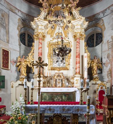 Zdjęcie nr 2: Nastawa ołtarzowa architektoniczna, jednoosiowa, jednokondygnacyjna ze zwieńczeniem z bramkami. Bramki z przejściami w formie stojącego prostokąta, zwieńczone fantazyjnym łukiem ujętym spływami wolutowymi, zakończonymi cokołami z figurami aniołów. Ołtarz kamienny w drewnianej obudowie z drewnianą mensą. Antepedium w formie leżącego prostokąta w profilowanej ramie, podzielone na pięć pól, w środkowym aplikowany monogram maryjny. Tabernakulum o wypukłej ścianie frontowej, ujęte w narożach ukośnie dostawionymi pilastrami o trzonach utworzonych z wolut. Drzwiczki w formie stojącego prostokąta zamkniętego łukiem wklęsło-wypukłym z uskokiem; w polu kielich z hostią w glorii. Tron wystawienia w formie zwężającego się ku górze cokołu o ściętych narożach, ujętych spływami wolutowymi. Z przodu owalny kartusz z monogramem IHS. Kondygnacja ustawiona na zdwojonym cokole, ujęta parą zwielokrotnionych pilastrów i parą kolumn wysuniętych do przodu o kapitelach kompozytowych, dźwigających imposty zwrócone do wewnątrz ołtarza oraz przerwany falisty przyczółek z siedzącą parą puttów. W polu środkowym profilowana rama w kształcie stojącego prostokąta z obrazem Matki Boskiej Częstochowskiej, na zasuwie obraz „Najświętsze Serce Jezusa”. Zwieńczenie w formie promienistej  glorii. W polu obłoki z otwartą księgą i uskrzydlonymi główkami anielskimi. Kondygnacja ujęta uszami utworzonymi z ażurowego ornamentu rocaille'owego z elementami wstęgi. Struktura polichromowana w kolorze beżowym, kolumny marmoryzowane w kolorze różowo-czerwonym, detale i ornamentyka złocone oraz srebrzone.