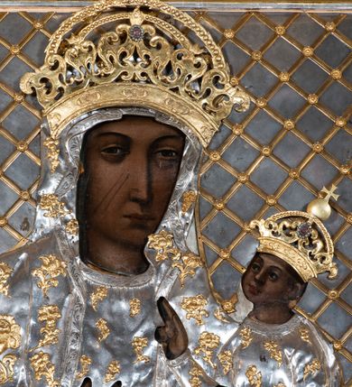 Zdjęcie nr 5: Obraz w formie stojącego prostokąta, w głębokiej, płaskorzeźbionej ramie z motywem liści i kartuszy. Matka Boska zwrócona delikatnie w lewo z Dzieciątkiem Jezus na lewej ręce, prawą na niego wskazująca. Twarz podłużna, z drobnymi ustami, długim i prostym nosem, nieco przymkniętymi oczami oraz dwiema szramami na prawym policzku. Dzieciątko zwrócone trzy czwarte prawo, lewą rączką podtrzymuje księgę, prawą błogosławi. Twarz o rysach dziecięcych z pulchnymi policzkami, z wyraźnie podkreślonymi oczami; karnacje ciemne. Na postacie nałożone metalowe sukienki, zdobione aplikowanymi, złoconymi, pojedynczymi kwiatkami. Maria i Dzieciątko mają nad głowami aplikowane, ażurowe korony zamknięte, zwieńczone kulą z krzyżykiem. Tło w postaci srebrnej blachy ze złoconą kratownicą. Rama drewniana, złocona i srebrzona, dekorowana pojedynczymi liśćmi oraz czterema płycinami zamkniętymi wolutkami. 