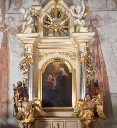 Zdjęcie nr 3: Ołtarz architektoniczny, przyścienny, jednoosiowy, jednokondygnacyjny, ze zwieńczeniem. Ołtarz drewniany, prostopadłościenny. Antepedium w kształcie leżącego prostokąta, ujęte profilowaną ramą, w polu płaskorzeźbiony grecki krzyżyk, a w narożach stylizowane wici akantu. W część cokołową wbudowane tabernakulum, z drzwiczkami ozdobionymi płaskorzeźbionym kielichem z hostią. Nastawa ustawiona na wysokim cokole, ujęta kolumnami o gładkich, posrebrzanych trzonach, z głowicami kompozytowymi, które podtrzymują silnie wysunięte do przodu wyłamane belkowanie ze wspólnym, bogato profilowanym, wysuniętym do przodu gzymsem. Na osi kolumn ponad gzymsem wolutowe przyczółki, na których siedzą uskrzydlone putta. W polu środkowym obraz w kształcie stojącego prostokąta, zamknięty łukiem nadwieszonym, ujęty w profilowaną ramę z przedstawieniem św. Anny Samotrzeć. Z przodu na tle kolumn ustawione dwie wolnostojące figury aniołów o złoconych skrzydłach i szatach. Po zewnętrznych stronach kolumn, na konsolach usadowione figury św. Józefa (po lewej) oraz św. Joachima (po prawej). Kondygnacja ujęta uszami ze stylizowanego ornamentu akantowego. 
Zwieńczenie flankowane półkolumnami o kompozytowych kapitelach podtrzymujących profilowany gzyms przybierający kształt dwóch stykających się wolut, zwieńczony muszlą palmetową i krzyżem. W polu zwieńczenia ażurowy prześwit w kształcie prostokąta o uskokowo i ćwierćkoliście ściętych narożach, wypełniony okiem Opatrzności na tle promienistej glorii. Struktura polichromowana w kolorze jasnego beżu, ornamentyka oraz detale złocone i srebrzone.