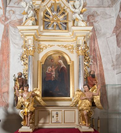 Zdjęcie nr 1: Ołtarz architektoniczny, przyścienny, jednoosiowy, jednokondygnacyjny, ze zwieńczeniem. Ołtarz drewniany, prostopadłościenny. Antepedium w kształcie leżącego prostokąta, ujęte profilowaną ramą, w polu płaskorzeźbiony grecki krzyżyk, a w narożach stylizowane wici akantu. W część cokołową wbudowane tabernakulum, z drzwiczkami ozdobionymi płaskorzeźbionym kielichem z hostią. Nastawa ustawiona na wysokim cokole, ujęta kolumnami o gładkich, posrebrzanych trzonach, z głowicami kompozytowymi, które podtrzymują silnie wysunięte do przodu wyłamane belkowanie ze wspólnym, bogato profilowanym, wysuniętym do przodu gzymsem. Na osi kolumn ponad gzymsem wolutowe przyczółki, na których siedzą uskrzydlone putta. W polu środkowym obraz w kształcie stojącego prostokąta, zamknięty łukiem nadwieszonym, ujęty w profilowaną ramę z przedstawieniem św. Anny Samotrzeć. Z przodu na tle kolumn ustawione dwie wolnostojące figury aniołów o złoconych skrzydłach i szatach. Po zewnętrznych stronach kolumn, na konsolach usadowione figury św. Józefa (po lewej) oraz św. Joachima (po prawej). Kondygnacja ujęta uszami ze stylizowanego ornamentu akantowego. 
Zwieńczenie flankowane półkolumnami o kompozytowych kapitelach podtrzymujących profilowany gzyms przybierający kształt dwóch stykających się wolut, zwieńczony muszlą palmetową i krzyżem. W polu zwieńczenia ażurowy prześwit w kształcie prostokąta o uskokowo i ćwierćkoliście ściętych narożach, wypełniony okiem Opatrzności na tle promienistej glorii. Struktura polichromowana w kolorze jasnego beżu, ornamentyka oraz detale złocone i srebrzone.