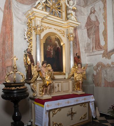 Zdjęcie nr 2: Ołtarz architektoniczny, przyścienny, jednoosiowy, jednokondygnacyjny, ze zwieńczeniem. Ołtarz drewniany, prostopadłościenny. Antepedium w kształcie leżącego prostokąta, ujęte profilowaną ramą, w polu płaskorzeźbiony grecki krzyżyk, a w narożach stylizowane wici akantu. W część cokołową wbudowane tabernakulum, z drzwiczkami ozdobionymi płaskorzeźbionym kielichem z hostią. Nastawa ustawiona na wysokim cokole, ujęta kolumnami o gładkich, posrebrzanych trzonach, z głowicami kompozytowymi, które podtrzymują silnie wysunięte do przodu wyłamane belkowanie ze wspólnym, bogato profilowanym, wysuniętym do przodu gzymsem. Na osi kolumn ponad gzymsem wolutowe przyczółki, na których siedzą uskrzydlone putta. W polu środkowym obraz w kształcie stojącego prostokąta, zamknięty łukiem nadwieszonym, ujęty w profilowaną ramę z przedstawieniem św. Anny Samotrzeć. Z przodu na tle kolumn ustawione dwie wolnostojące figury aniołów o złoconych skrzydłach i szatach. Po zewnętrznych stronach kolumn, na konsolach usadowione figury św. Józefa (po lewej) oraz św. Joachima (po prawej). Kondygnacja ujęta uszami ze stylizowanego ornamentu akantowego. 
Zwieńczenie flankowane półkolumnami o kompozytowych kapitelach podtrzymujących profilowany gzyms przybierający kształt dwóch stykających się wolut, zwieńczony muszlą palmetową i krzyżem. W polu zwieńczenia ażurowy prześwit w kształcie prostokąta o uskokowo i ćwierćkoliście ściętych narożach, wypełniony okiem Opatrzności na tle promienistej glorii. Struktura polichromowana w kolorze jasnego beżu, ornamentyka oraz detale złocone i srebrzone.