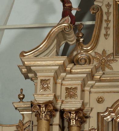 Zdjęcie nr 16: Ołtarz architektoniczny, jednokondygnacyjny, trójosiowy, ze zwieńczeniem. Ołtarz prostopadłościenny, z drewnianą mensą. Antepedium w formie haftowanej tkaniny zdobionej po środku motywem zwieńczonego krzyżem monogramu maryjnego z koroną, ujętego dwunastoma gwiazdami, natomiast w dolnych narożach gałązkami z kwiatami białych lilii.  Tabernakulum z tronem wystawienia w formie jednokondygnacyjnej, trójosiowej bryły architektonicznej, osadzonej na wysokim cokole. Tabernakulum wbudowane w osi środkowej cokołu, drzwiczki prostokątne, zdobione płaskorzeźbionym motywem kielicha eucharystycznego. Flankowane po skrajnych bokach parą pilastrów osie boczne całej struktury są wklęsłe i cofnięte względem osi środkowej ujętej parą kolumienek. Podpory wspierają wyłamujące się ponad nimi belkowanie z gzymsem po środku w formie łuku koszowego. Część środkowa w formie niszy zamkniętej motywem konchy. W zwieńczeniu figurka baranka paschalnego ujętego promienistą glorią, ukazanego na owalnej podstawie osadzonej na 4 wolutowych kabłąkach. Po bokach para figur adorujących aniołów. Cokół zdobiony motywami uskrzydlonych główek anielskich, rocaille’i oraz gałązek z kiściami winnej latorośli. Pola osi bocznych wypełnia para podwieszeń w formie gałązek różanych, partie fryzu pojedyncze rozetki. Struktura tabernakulum i tronu wystawienia jest złocona i srebrzona.   Retabulum osadzone na zdwojonym, zryzalitowanym uskokowo po bokach cokole. Część środkowa ujęta dwoma parami kolumn – wewnętrzne ustawione na tle pary pilastrów, zewnętrzne na tle pary filarów. Podpory dźwigają wyłamujące się ponad nimi belkowanie przerwane w partii architrawu i fryzu. Zwieńczenie ujęte parą spływów wolutowych, zamknięte parą stykających się wolut. Po bokach przerwany, wolutowy przyczółek. W dolnych polach osi bocznych retabulum para półkoliście zamkniętych bramek, ujętych prostą arkadą. Pola osi oddzielone parami stykających się wolut zwieńczonych konchą. W górnej strefie para płytkich niszy zamkniętych półkolistymi łukami nadwieszonymi i dodatkowo ujęta prostym, trójkątnie zamkniętym obramieniem. Osie zwieńczone trzema fragmentami gzymsu oddzielonymi parami wklęsłości.  Pola cokołu osi środkowej retabulum wypełnione ornamentyką roślinną. Część środkowa ujęta parą ażurowych, ornamentalnych  uszaków. Po bokach pola para zwisów w postaci gałązek różanych, w górnych narożach para rozetek. Pola fryzu zdobione rozetami. Pole zwieńczenia w górnej partii dekorowane parą ulistnionych gałązek, po bokach parą kampanuli, dołem w narożach para dużych rozet, pośrodku wić roślinna. Na spływach wolutowych para płomienistych wazonów, a na przyczółku para figur aniołów. Nadłucza bramek osi bocznych zdobione ornamentem roślinnym, nisze ujęte parą stylizowanych kandelabrów, wyżej para rombów z rozetami, pośrodku gwiazda. Na gzymsach wieńczących płomieniste wazony. W polu środkowym obraz w kształcie stojącego prostokąta zamkniętego odcinkowym łukiem nadwieszonym z uskokami, z wizerunkiem Madonny z Dzieciątkiem. W zwieńczeniu obraz w kształcie stojącego prostokąta zamkniętego odcinkowym łukiem nadwieszonym z uskokami, z wizerunkiem Chrystusa Króla. Nisze osi bocznych wypełniają figury, po prawej stronie św. Barbary, po lewej nieznanej świętej. Struktura w kolorze beżowym, detal architektoniczny i ornamentyka złocone.     