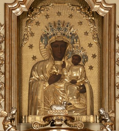 Zdjęcie nr 19: Ołtarz architektoniczny, jednokondygnacyjny, trójosiowy, ze zwieńczeniem. Ołtarz prostopadłościenny, z drewnianą mensą. Antepedium w formie haftowanej tkaniny zdobionej po środku motywem zwieńczonego krzyżem monogramu maryjnego z koroną, ujętego dwunastoma gwiazdami, natomiast w dolnych narożach gałązkami z kwiatami białych lilii.  Tabernakulum z tronem wystawienia w formie jednokondygnacyjnej, trójosiowej bryły architektonicznej, osadzonej na wysokim cokole. Tabernakulum wbudowane w osi środkowej cokołu, drzwiczki prostokątne, zdobione płaskorzeźbionym motywem kielicha eucharystycznego. Flankowane po skrajnych bokach parą pilastrów osie boczne całej struktury są wklęsłe i cofnięte względem osi środkowej ujętej parą kolumienek. Podpory wspierają wyłamujące się ponad nimi belkowanie z gzymsem po środku w formie łuku koszowego. Część środkowa w formie niszy zamkniętej motywem konchy. W zwieńczeniu figurka baranka paschalnego ujętego promienistą glorią, ukazanego na owalnej podstawie osadzonej na 4 wolutowych kabłąkach. Po bokach para figur adorujących aniołów. Cokół zdobiony motywami uskrzydlonych główek anielskich, rocaille’i oraz gałązek z kiściami winnej latorośli. Pola osi bocznych wypełnia para podwieszeń w formie gałązek różanych, partie fryzu pojedyncze rozetki. Struktura tabernakulum i tronu wystawienia jest złocona i srebrzona.   Retabulum osadzone na zdwojonym, zryzalitowanym uskokowo po bokach cokole. Część środkowa ujęta dwoma parami kolumn – wewnętrzne ustawione na tle pary pilastrów, zewnętrzne na tle pary filarów. Podpory dźwigają wyłamujące się ponad nimi belkowanie przerwane w partii architrawu i fryzu. Zwieńczenie ujęte parą spływów wolutowych, zamknięte parą stykających się wolut. Po bokach przerwany, wolutowy przyczółek. W dolnych polach osi bocznych retabulum para półkoliście zamkniętych bramek, ujętych prostą arkadą. Pola osi oddzielone parami stykających się wolut zwieńczonych konchą. W górnej strefie para płytkich niszy zamkniętych półkolistymi łukami nadwieszonymi i dodatkowo ujęta prostym, trójkątnie zamkniętym obramieniem. Osie zwieńczone trzema fragmentami gzymsu oddzielonymi parami wklęsłości.  Pola cokołu osi środkowej retabulum wypełnione ornamentyką roślinną. Część środkowa ujęta parą ażurowych, ornamentalnych  uszaków. Po bokach pola para zwisów w postaci gałązek różanych, w górnych narożach para rozetek. Pola fryzu zdobione rozetami. Pole zwieńczenia w górnej partii dekorowane parą ulistnionych gałązek, po bokach parą kampanuli, dołem w narożach para dużych rozet, pośrodku wić roślinna. Na spływach wolutowych para płomienistych wazonów, a na przyczółku para figur aniołów. Nadłucza bramek osi bocznych zdobione ornamentem roślinnym, nisze ujęte parą stylizowanych kandelabrów, wyżej para rombów z rozetami, pośrodku gwiazda. Na gzymsach wieńczących płomieniste wazony. W polu środkowym obraz w kształcie stojącego prostokąta zamkniętego odcinkowym łukiem nadwieszonym z uskokami, z wizerunkiem Madonny z Dzieciątkiem. W zwieńczeniu obraz w kształcie stojącego prostokąta zamkniętego odcinkowym łukiem nadwieszonym z uskokami, z wizerunkiem Chrystusa Króla. Nisze osi bocznych wypełniają figury, po prawej stronie św. Barbary, po lewej nieznanej świętej. Struktura w kolorze beżowym, detal architektoniczny i ornamentyka złocone.     