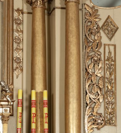 Zdjęcie nr 4: Ołtarz architektoniczny, jednokondygnacyjny, trójosiowy, ze zwieńczeniem. Ołtarz prostopadłościenny, z drewnianą mensą. Antepedium w formie haftowanej tkaniny zdobionej po środku motywem zwieńczonego krzyżem monogramu maryjnego z koroną, ujętego dwunastoma gwiazdami, natomiast w dolnych narożach gałązkami z kwiatami białych lilii.  Tabernakulum z tronem wystawienia w formie jednokondygnacyjnej, trójosiowej bryły architektonicznej, osadzonej na wysokim cokole. Tabernakulum wbudowane w osi środkowej cokołu, drzwiczki prostokątne, zdobione płaskorzeźbionym motywem kielicha eucharystycznego. Flankowane po skrajnych bokach parą pilastrów osie boczne całej struktury są wklęsłe i cofnięte względem osi środkowej ujętej parą kolumienek. Podpory wspierają wyłamujące się ponad nimi belkowanie z gzymsem po środku w formie łuku koszowego. Część środkowa w formie niszy zamkniętej motywem konchy. W zwieńczeniu figurka baranka paschalnego ujętego promienistą glorią, ukazanego na owalnej podstawie osadzonej na 4 wolutowych kabłąkach. Po bokach para figur adorujących aniołów. Cokół zdobiony motywami uskrzydlonych główek anielskich, rocaille’i oraz gałązek z kiściami winnej latorośli. Pola osi bocznych wypełnia para podwieszeń w formie gałązek różanych, partie fryzu pojedyncze rozetki. Struktura tabernakulum i tronu wystawienia jest złocona i srebrzona.   Retabulum osadzone na zdwojonym, zryzalitowanym uskokowo po bokach cokole. Część środkowa ujęta dwoma parami kolumn – wewnętrzne ustawione na tle pary pilastrów, zewnętrzne na tle pary filarów. Podpory dźwigają wyłamujące się ponad nimi belkowanie przerwane w partii architrawu i fryzu. Zwieńczenie ujęte parą spływów wolutowych, zamknięte parą stykających się wolut. Po bokach przerwany, wolutowy przyczółek. W dolnych polach osi bocznych retabulum para półkoliście zamkniętych bramek, ujętych prostą arkadą. Pola osi oddzielone parami stykających się wolut zwieńczonych konchą. W górnej strefie para płytkich niszy zamkniętych półkolistymi łukami nadwieszonymi i dodatkowo ujęta prostym, trójkątnie zamkniętym obramieniem. Osie zwieńczone trzema fragmentami gzymsu oddzielonymi parami wklęsłości.  Pola cokołu osi środkowej retabulum wypełnione ornamentyką roślinną. Część środkowa ujęta parą ażurowych, ornamentalnych  uszaków. Po bokach pola para zwisów w postaci gałązek różanych, w górnych narożach para rozetek. Pola fryzu zdobione rozetami. Pole zwieńczenia w górnej partii dekorowane parą ulistnionych gałązek, po bokach parą kampanuli, dołem w narożach para dużych rozet, pośrodku wić roślinna. Na spływach wolutowych para płomienistych wazonów, a na przyczółku para figur aniołów. Nadłucza bramek osi bocznych zdobione ornamentem roślinnym, nisze ujęte parą stylizowanych kandelabrów, wyżej para rombów z rozetami, pośrodku gwiazda. Na gzymsach wieńczących płomieniste wazony. W polu środkowym obraz w kształcie stojącego prostokąta zamkniętego odcinkowym łukiem nadwieszonym z uskokami, z wizerunkiem Madonny z Dzieciątkiem. W zwieńczeniu obraz w kształcie stojącego prostokąta zamkniętego odcinkowym łukiem nadwieszonym z uskokami, z wizerunkiem Chrystusa Króla. Nisze osi bocznych wypełniają figury, po prawej stronie św. Barbary, po lewej nieznanej świętej. Struktura w kolorze beżowym, detal architektoniczny i ornamentyka złocone.     