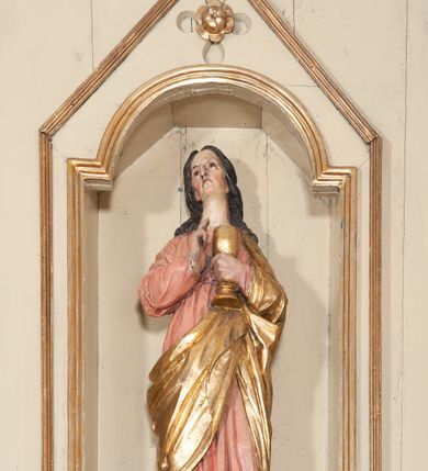 Zdjęcie nr 14: Ołtarz architektoniczny, jednokondygnacyjny, trójosiowy, ze zwieńczeniem. Ołtarz prostopadłościenny, z drewnianą mensą. Antepedium w formie haftowanej tkaniny zdobionej po środku motywem zwieńczonego krzyżem monogramu maryjnego z koroną, ujętego dwunastoma gwiazdami, natomiast w dolnych narożach gałązkami z kwiatami białych lilii.  Tabernakulum z tronem wystawienia w formie jednokondygnacyjnej, trójosiowej bryły architektonicznej, osadzonej na wysokim cokole. Tabernakulum wbudowane w osi środkowej cokołu, drzwiczki prostokątne, zdobione płaskorzeźbionym motywem kielicha eucharystycznego. Flankowane po skrajnych bokach parą pilastrów osie boczne całej struktury są wklęsłe i cofnięte względem osi środkowej ujętej parą kolumienek. Podpory wspierają wyłamujące się ponad nimi belkowanie z gzymsem po środku w formie łuku koszowego. Część środkowa w formie niszy zamkniętej motywem konchy. W zwieńczeniu figurka baranka paschalnego ujętego promienistą glorią, ukazanego na owalnej podstawie osadzonej na 4 wolutowych kabłąkach. Po bokach para figur adorujących aniołów. Cokół zdobiony motywami uskrzydlonych główek anielskich, rocaille’i oraz gałązek z kiściami winnej latorośli. Pola osi bocznych wypełnia para podwieszeń w formie gałązek różanych, partie fryzu pojedyncze rozetki. Struktura tabernakulum i tronu wystawienia jest złocona i srebrzona.   Retabulum osadzone na zdwojonym, zryzalitowanym uskokowo po bokach cokole. Część środkowa ujęta dwoma parami kolumn – wewnętrzne ustawione na tle pary pilastrów, zewnętrzne na tle pary filarów. Podpory dźwigają wyłamujące się ponad nimi belkowanie przerwane w partii architrawu i fryzu. Zwieńczenie ujęte parą spływów wolutowych, zamknięte parą stykających się wolut. Po bokach przerwany, wolutowy przyczółek. W dolnych polach osi bocznych retabulum para półkoliście zamkniętych bramek, ujętych prostą arkadą. Pola osi oddzielone parami stykających się wolut zwieńczonych konchą. W górnej strefie para płytkich niszy zamkniętych półkolistymi łukami nadwieszonymi i dodatkowo ujęta prostym, trójkątnie zamkniętym obramieniem. Osie zwieńczone trzema fragmentami gzymsu oddzielonymi parami wklęsłości.  Pola cokołu osi środkowej retabulum wypełnione ornamentyką roślinną. Część środkowa ujęta parą ażurowych, ornamentalnych  uszaków. Po bokach pola para zwisów w postaci gałązek różanych, w górnych narożach para rozetek. Pola fryzu zdobione rozetami. Pole zwieńczenia w górnej partii dekorowane parą ulistnionych gałązek, po bokach parą kampanuli, dołem w narożach para dużych rozet, pośrodku wić roślinna. Na spływach wolutowych para płomienistych wazonów, a na przyczółku para figur aniołów. Nadłucza bramek osi bocznych zdobione ornamentem roślinnym, nisze ujęte parą stylizowanych kandelabrów, wyżej para rombów z rozetami, pośrodku gwiazda. Na gzymsach wieńczących płomieniste wazony. W polu środkowym obraz w kształcie stojącego prostokąta zamkniętego odcinkowym łukiem nadwieszonym z uskokami, z wizerunkiem Madonny z Dzieciątkiem. W zwieńczeniu obraz w kształcie stojącego prostokąta zamkniętego odcinkowym łukiem nadwieszonym z uskokami, z wizerunkiem Chrystusa Króla. Nisze osi bocznych wypełniają figury, po prawej stronie św. Barbary, po lewej nieznanej świętej. Struktura w kolorze beżowym, detal architektoniczny i ornamentyka złocone.     