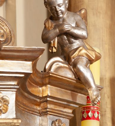 Zdjęcie nr 10: Ołtarz architektoniczny, jednokondygnacyjny, trójosiowy, ze zwieńczeniem. Ołtarz prostopadłościenny, z drewnianą mensą. Antepedium w formie haftowanej tkaniny zdobionej po środku motywem zwieńczonego krzyżem monogramu maryjnego z koroną, ujętego dwunastoma gwiazdami, natomiast w dolnych narożach gałązkami z kwiatami białych lilii.  Tabernakulum z tronem wystawienia w formie jednokondygnacyjnej, trójosiowej bryły architektonicznej, osadzonej na wysokim cokole. Tabernakulum wbudowane w osi środkowej cokołu, drzwiczki prostokątne, zdobione płaskorzeźbionym motywem kielicha eucharystycznego. Flankowane po skrajnych bokach parą pilastrów osie boczne całej struktury są wklęsłe i cofnięte względem osi środkowej ujętej parą kolumienek. Podpory wspierają wyłamujące się ponad nimi belkowanie z gzymsem po środku w formie łuku koszowego. Część środkowa w formie niszy zamkniętej motywem konchy. W zwieńczeniu figurka baranka paschalnego ujętego promienistą glorią, ukazanego na owalnej podstawie osadzonej na 4 wolutowych kabłąkach. Po bokach para figur adorujących aniołów. Cokół zdobiony motywami uskrzydlonych główek anielskich, rocaille’i oraz gałązek z kiściami winnej latorośli. Pola osi bocznych wypełnia para podwieszeń w formie gałązek różanych, partie fryzu pojedyncze rozetki. Struktura tabernakulum i tronu wystawienia jest złocona i srebrzona.   Retabulum osadzone na zdwojonym, zryzalitowanym uskokowo po bokach cokole. Część środkowa ujęta dwoma parami kolumn – wewnętrzne ustawione na tle pary pilastrów, zewnętrzne na tle pary filarów. Podpory dźwigają wyłamujące się ponad nimi belkowanie przerwane w partii architrawu i fryzu. Zwieńczenie ujęte parą spływów wolutowych, zamknięte parą stykających się wolut. Po bokach przerwany, wolutowy przyczółek. W dolnych polach osi bocznych retabulum para półkoliście zamkniętych bramek, ujętych prostą arkadą. Pola osi oddzielone parami stykających się wolut zwieńczonych konchą. W górnej strefie para płytkich niszy zamkniętych półkolistymi łukami nadwieszonymi i dodatkowo ujęta prostym, trójkątnie zamkniętym obramieniem. Osie zwieńczone trzema fragmentami gzymsu oddzielonymi parami wklęsłości.  Pola cokołu osi środkowej retabulum wypełnione ornamentyką roślinną. Część środkowa ujęta parą ażurowych, ornamentalnych  uszaków. Po bokach pola para zwisów w postaci gałązek różanych, w górnych narożach para rozetek. Pola fryzu zdobione rozetami. Pole zwieńczenia w górnej partii dekorowane parą ulistnionych gałązek, po bokach parą kampanuli, dołem w narożach para dużych rozet, pośrodku wić roślinna. Na spływach wolutowych para płomienistych wazonów, a na przyczółku para figur aniołów. Nadłucza bramek osi bocznych zdobione ornamentem roślinnym, nisze ujęte parą stylizowanych kandelabrów, wyżej para rombów z rozetami, pośrodku gwiazda. Na gzymsach wieńczących płomieniste wazony. W polu środkowym obraz w kształcie stojącego prostokąta zamkniętego odcinkowym łukiem nadwieszonym z uskokami, z wizerunkiem Madonny z Dzieciątkiem. W zwieńczeniu obraz w kształcie stojącego prostokąta zamkniętego odcinkowym łukiem nadwieszonym z uskokami, z wizerunkiem Chrystusa Króla. Nisze osi bocznych wypełniają figury, po prawej stronie św. Barbary, po lewej nieznanej świętej. Struktura w kolorze beżowym, detal architektoniczny i ornamentyka złocone.     