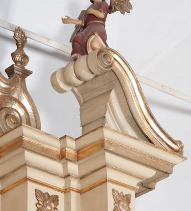 Zdjęcie nr 12: Ołtarz architektoniczny, jednokondygnacyjny, trójosiowy, ze zwieńczeniem. Ołtarz prostopadłościenny, z drewnianą mensą. Antepedium w formie haftowanej tkaniny zdobionej po środku motywem zwieńczonego krzyżem monogramu maryjnego z koroną, ujętego dwunastoma gwiazdami, natomiast w dolnych narożach gałązkami z kwiatami białych lilii.  Tabernakulum z tronem wystawienia w formie jednokondygnacyjnej, trójosiowej bryły architektonicznej, osadzonej na wysokim cokole. Tabernakulum wbudowane w osi środkowej cokołu, drzwiczki prostokątne, zdobione płaskorzeźbionym motywem kielicha eucharystycznego. Flankowane po skrajnych bokach parą pilastrów osie boczne całej struktury są wklęsłe i cofnięte względem osi środkowej ujętej parą kolumienek. Podpory wspierają wyłamujące się ponad nimi belkowanie z gzymsem po środku w formie łuku koszowego. Część środkowa w formie niszy zamkniętej motywem konchy. W zwieńczeniu figurka baranka paschalnego ujętego promienistą glorią, ukazanego na owalnej podstawie osadzonej na 4 wolutowych kabłąkach. Po bokach para figur adorujących aniołów. Cokół zdobiony motywami uskrzydlonych główek anielskich, rocaille’i oraz gałązek z kiściami winnej latorośli. Pola osi bocznych wypełnia para podwieszeń w formie gałązek różanych, partie fryzu pojedyncze rozetki. Struktura tabernakulum i tronu wystawienia jest złocona i srebrzona.   Retabulum osadzone na zdwojonym, zryzalitowanym uskokowo po bokach cokole. Część środkowa ujęta dwoma parami kolumn – wewnętrzne ustawione na tle pary pilastrów, zewnętrzne na tle pary filarów. Podpory dźwigają wyłamujące się ponad nimi belkowanie przerwane w partii architrawu i fryzu. Zwieńczenie ujęte parą spływów wolutowych, zamknięte parą stykających się wolut. Po bokach przerwany, wolutowy przyczółek. W dolnych polach osi bocznych retabulum para półkoliście zamkniętych bramek, ujętych prostą arkadą. Pola osi oddzielone parami stykających się wolut zwieńczonych konchą. W górnej strefie para płytkich niszy zamkniętych półkolistymi łukami nadwieszonymi i dodatkowo ujęta prostym, trójkątnie zamkniętym obramieniem. Osie zwieńczone trzema fragmentami gzymsu oddzielonymi parami wklęsłości.  Pola cokołu osi środkowej retabulum wypełnione ornamentyką roślinną. Część środkowa ujęta parą ażurowych, ornamentalnych  uszaków. Po bokach pola para zwisów w postaci gałązek różanych, w górnych narożach para rozetek. Pola fryzu zdobione rozetami. Pole zwieńczenia w górnej partii dekorowane parą ulistnionych gałązek, po bokach parą kampanuli, dołem w narożach para dużych rozet, pośrodku wić roślinna. Na spływach wolutowych para płomienistych wazonów, a na przyczółku para figur aniołów. Nadłucza bramek osi bocznych zdobione ornamentem roślinnym, nisze ujęte parą stylizowanych kandelabrów, wyżej para rombów z rozetami, pośrodku gwiazda. Na gzymsach wieńczących płomieniste wazony. W polu środkowym obraz w kształcie stojącego prostokąta zamkniętego odcinkowym łukiem nadwieszonym z uskokami, z wizerunkiem Madonny z Dzieciątkiem. W zwieńczeniu obraz w kształcie stojącego prostokąta zamkniętego odcinkowym łukiem nadwieszonym z uskokami, z wizerunkiem Chrystusa Króla. Nisze osi bocznych wypełniają figury, po prawej stronie św. Barbary, po lewej nieznanej świętej. Struktura w kolorze beżowym, detal architektoniczny i ornamentyka złocone.     