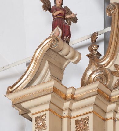 Zdjęcie nr 11: Ołtarz architektoniczny, jednokondygnacyjny, trójosiowy, ze zwieńczeniem. Ołtarz prostopadłościenny, z drewnianą mensą. Antepedium w formie haftowanej tkaniny zdobionej po środku motywem zwieńczonego krzyżem monogramu maryjnego z koroną, ujętego dwunastoma gwiazdami, natomiast w dolnych narożach gałązkami z kwiatami białych lilii.  Tabernakulum z tronem wystawienia w formie jednokondygnacyjnej, trójosiowej bryły architektonicznej, osadzonej na wysokim cokole. Tabernakulum wbudowane w osi środkowej cokołu, drzwiczki prostokątne, zdobione płaskorzeźbionym motywem kielicha eucharystycznego. Flankowane po skrajnych bokach parą pilastrów osie boczne całej struktury są wklęsłe i cofnięte względem osi środkowej ujętej parą kolumienek. Podpory wspierają wyłamujące się ponad nimi belkowanie z gzymsem po środku w formie łuku koszowego. Część środkowa w formie niszy zamkniętej motywem konchy. W zwieńczeniu figurka baranka paschalnego ujętego promienistą glorią, ukazanego na owalnej podstawie osadzonej na 4 wolutowych kabłąkach. Po bokach para figur adorujących aniołów. Cokół zdobiony motywami uskrzydlonych główek anielskich, rocaille’i oraz gałązek z kiściami winnej latorośli. Pola osi bocznych wypełnia para podwieszeń w formie gałązek różanych, partie fryzu pojedyncze rozetki. Struktura tabernakulum i tronu wystawienia jest złocona i srebrzona.   Retabulum osadzone na zdwojonym, zryzalitowanym uskokowo po bokach cokole. Część środkowa ujęta dwoma parami kolumn – wewnętrzne ustawione na tle pary pilastrów, zewnętrzne na tle pary filarów. Podpory dźwigają wyłamujące się ponad nimi belkowanie przerwane w partii architrawu i fryzu. Zwieńczenie ujęte parą spływów wolutowych, zamknięte parą stykających się wolut. Po bokach przerwany, wolutowy przyczółek. W dolnych polach osi bocznych retabulum para półkoliście zamkniętych bramek, ujętych prostą arkadą. Pola osi oddzielone parami stykających się wolut zwieńczonych konchą. W górnej strefie para płytkich niszy zamkniętych półkolistymi łukami nadwieszonymi i dodatkowo ujęta prostym, trójkątnie zamkniętym obramieniem. Osie zwieńczone trzema fragmentami gzymsu oddzielonymi parami wklęsłości.  Pola cokołu osi środkowej retabulum wypełnione ornamentyką roślinną. Część środkowa ujęta parą ażurowych, ornamentalnych  uszaków. Po bokach pola para zwisów w postaci gałązek różanych, w górnych narożach para rozetek. Pola fryzu zdobione rozetami. Pole zwieńczenia w górnej partii dekorowane parą ulistnionych gałązek, po bokach parą kampanuli, dołem w narożach para dużych rozet, pośrodku wić roślinna. Na spływach wolutowych para płomienistych wazonów, a na przyczółku para figur aniołów. Nadłucza bramek osi bocznych zdobione ornamentem roślinnym, nisze ujęte parą stylizowanych kandelabrów, wyżej para rombów z rozetami, pośrodku gwiazda. Na gzymsach wieńczących płomieniste wazony. W polu środkowym obraz w kształcie stojącego prostokąta zamkniętego odcinkowym łukiem nadwieszonym z uskokami, z wizerunkiem Madonny z Dzieciątkiem. W zwieńczeniu obraz w kształcie stojącego prostokąta zamkniętego odcinkowym łukiem nadwieszonym z uskokami, z wizerunkiem Chrystusa Króla. Nisze osi bocznych wypełniają figury, po prawej stronie św. Barbary, po lewej nieznanej świętej. Struktura w kolorze beżowym, detal architektoniczny i ornamentyka złocone.     