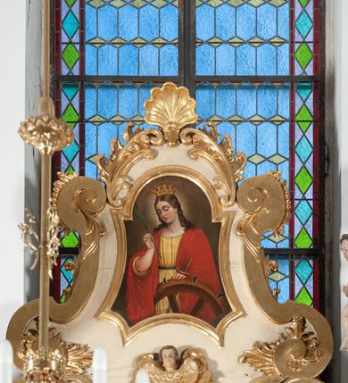 Zdjęcie nr 26: Ołtarz architektoniczny, jednokondygnacyjny, jednoosiowy ze zwieńczeniem. Ołtarz prostopadłościenny, z drewnianą mensą, z antepedium ujętym po bokach parą konsoli w formie wolut. Pole antepedium w postaci prostokątnej płyciny z płaskorzeźbionym motywem gorejącego serca pośrodku, ujętego promienistą glorią. Na mensie tabernakulum w formie prostopadłościennej szafki o wypukłej, przedniej  ściance ujętej dwoma parami osadzonych na niewielkich cokołach kolumienek wspierających niepełne, wyłamujące się ponad nimi belkowanie. Drzwiczki w kształcie stojącego prostokąta zamkniętego półkolistym łukiem nadwieszonym, zdobione motywem płaskorzeźbionego kielicha eucharystycznego. Struktura zdobiona motywami rozet i wici roślinnej. Retabulum osadzone na niewysokim, zryzalitowanym po bokach cokole. Część środkową nastawy ujmuje para ustawionych skośnie  filarów wspierających wyłamujące się ponad nimi belkowanie. Zamknięte półkoliście zwieńczenie ujmuje para spływów wolutowych oraz flankuje przerwany, wolutowy przyczółek. Pola wolutowych konsoli zdobi para liści akantu, cokół retabulum para stylizowanych słoneczników i S-kształtnych wici. Zewnętrzne pola trzonów filarów zdobią w górnych partiach ukwiecone gałązki, wewnętrzne motyw podwieszeń skomponowanych z zamkniętej korony, krzyżujących się rogów obfitości i krzyża z kotwicą, oraz kokard, u dołu para gałązek. Boki pola środkowego z motywem wici winnego grona, u góry w narożach para ulistnionych rozet. Fryz zdobiony rozetami, pośrodku kartusz w monogramem imienia Jezus ujętym parą gałązek laurowych. Retabulum flankowane parą ażurowych uszaków rocaille’owych. W dolnej partii zwieńczenia uskrzydlona główka anielska, szczyt w formie konchy ujętej po bokach parą rocaille’i. Na przerwanym przyczółku para figur aniołków. Pole części środkowej w kształcie stojącego prostokąta zamkniętego półkolistym łukiem nadwieszonym z uskokami, ujęte profilowaną, złoconą ramą, w środku wizerunek Najświętszego Serca Jezusa. Po bokach, na tle filarów para figur, po lewej św. Szczepan, po prawej św. Wawrzyniec. W zwieńczeniu obraz w kształcie trapezu o wklęsłych ramionach, podstawie i dolnych narożach, zamknięty półkolistym łukiem nadwieszonym, ujęty profilowaną, złoconą ramą, z wizerunkiem św. Katarzyny Aleksandryjskiej. 
Struktura w kolorze kremowym, detal architektoniczny i ornamentyka złocone.    
