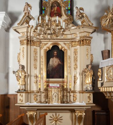 Zdjęcie nr 1: Ołtarz architektoniczny, jednokondygnacyjny, jednoosiowy ze zwieńczeniem. Ołtarz prostopadłościenny, z drewnianą mensą, z antepedium ujętym po bokach parą konsoli w formie wolut. Pole antepedium w postaci prostokątnej płyciny z płaskorzeźbionym motywem gorejącego serca pośrodku, ujętego promienistą glorią. Na mensie tabernakulum w formie prostopadłościennej szafki o wypukłej, przedniej  ściance ujętej dwoma parami osadzonych na niewielkich cokołach kolumienek wspierających niepełne, wyłamujące się ponad nimi belkowanie. Drzwiczki w kształcie stojącego prostokąta zamkniętego półkolistym łukiem nadwieszonym, zdobione motywem płaskorzeźbionego kielicha eucharystycznego. Struktura zdobiona motywami rozet i wici roślinnej. Retabulum osadzone na niewysokim, zryzalitowanym po bokach cokole. Część środkową nastawy ujmuje para ustawionych skośnie  filarów wspierających wyłamujące się ponad nimi belkowanie. Zamknięte półkoliście zwieńczenie ujmuje para spływów wolutowych oraz flankuje przerwany, wolutowy przyczółek. Pola wolutowych konsoli zdobi para liści akantu, cokół retabulum para stylizowanych słoneczników i S-kształtnych wici. Zewnętrzne pola trzonów filarów zdobią w górnych partiach ukwiecone gałązki, wewnętrzne motyw podwieszeń skomponowanych z zamkniętej korony, krzyżujących się rogów obfitości i krzyża z kotwicą, oraz kokard, u dołu para gałązek. Boki pola środkowego z motywem wici winnego grona, u góry w narożach para ulistnionych rozet. Fryz zdobiony rozetami, pośrodku kartusz w monogramem imienia Jezus ujętym parą gałązek laurowych. Retabulum flankowane parą ażurowych uszaków rocaille’owych. W dolnej partii zwieńczenia uskrzydlona główka anielska, szczyt w formie konchy ujętej po bokach parą rocaille’i. Na przerwanym przyczółku para figur aniołków. Pole części środkowej w kształcie stojącego prostokąta zamkniętego półkolistym łukiem nadwieszonym z uskokami, ujęte profilowaną, złoconą ramą, w środku wizerunek Najświętszego Serca Jezusa. Po bokach, na tle filarów para figur, po lewej św. Szczepan, po prawej św. Wawrzyniec. W zwieńczeniu obraz w kształcie trapezu o wklęsłych ramionach, podstawie i dolnych narożach, zamknięty półkolistym łukiem nadwieszonym, ujęty profilowaną, złoconą ramą, z wizerunkiem św. Katarzyny Aleksandryjskiej. 
Struktura w kolorze kremowym, detal architektoniczny i ornamentyka złocone.    

