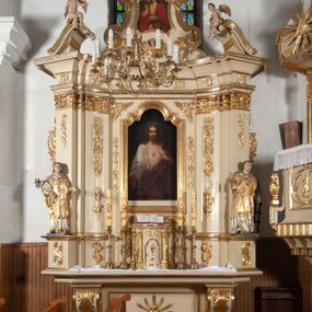 Zdjęcie nr 1: Ołtarz architektoniczny, jednokondygnacyjny, jednoosiowy ze zwieńczeniem. Ołtarz prostopadłościenny, z drewnianą mensą, z antepedium ujętym po bokach parą konsoli w formie wolut. Pole antepedium w postaci prostokątnej płyciny z płaskorzeźbionym motywem gorejącego serca pośrodku, ujętego promienistą glorią. Na mensie tabernakulum w formie prostopadłościennej szafki o wypukłej, przedniej  ściance ujętej dwoma parami osadzonych na niewielkich cokołach kolumienek wspierających niepełne, wyłamujące się ponad nimi belkowanie. Drzwiczki w kształcie stojącego prostokąta zamkniętego półkolistym łukiem nadwieszonym, zdobione motywem płaskorzeźbionego kielicha eucharystycznego. Struktura zdobiona motywami rozet i wici roślinnej. Retabulum osadzone na niewysokim, zryzalitowanym po bokach cokole. Część środkową nastawy ujmuje para ustawionych skośnie  filarów wspierających wyłamujące się ponad nimi belkowanie. Zamknięte półkoliście zwieńczenie ujmuje para spływów wolutowych oraz flankuje przerwany, wolutowy przyczółek. Pola wolutowych konsoli zdobi para liści akantu, cokół retabulum para stylizowanych słoneczników i S-kształtnych wici. Zewnętrzne pola trzonów filarów zdobią w górnych partiach ukwiecone gałązki, wewnętrzne motyw podwieszeń skomponowanych z zamkniętej korony, krzyżujących się rogów obfitości i krzyża z kotwicą, oraz kokard, u dołu para gałązek. Boki pola środkowego z motywem wici winnego grona, u góry w narożach para ulistnionych rozet. Fryz zdobiony rozetami, pośrodku kartusz w monogramem imienia Jezus ujętym parą gałązek laurowych. Retabulum flankowane parą ażurowych uszaków rocaille’owych. W dolnej partii zwieńczenia uskrzydlona główka anielska, szczyt w formie konchy ujętej po bokach parą rocaille’i. Na przerwanym przyczółku para figur aniołków. Pole części środkowej w kształcie stojącego prostokąta zamkniętego półkolistym łukiem nadwieszonym z uskokami, ujęte profilowaną, złoconą ramą, w środku wizerunek Najświętszego Serca Jezusa. Po bokach, na tle filarów para figur, po lewej św. Szczepan, po prawej św. Wawrzyniec. W zwieńczeniu obraz w kształcie trapezu o wklęsłych ramionach, podstawie i dolnych narożach, zamknięty półkolistym łukiem nadwieszonym, ujęty profilowaną, złoconą ramą, z wizerunkiem św. Katarzyny Aleksandryjskiej. 
Struktura w kolorze kremowym, detal architektoniczny i ornamentyka złocone.    

