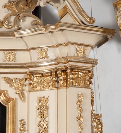 Zdjęcie nr 29: Ołtarz architektoniczny, jednokondygnacyjny, jednoosiowy ze zwieńczeniem. Ołtarz prostopadłościenny, z drewnianą mensą, z antepedium ujętym po bokach parą konsoli w formie wolut. Pole antepedium w postaci prostokątnej płyciny z płaskorzeźbionym motywem gorejącego serca pośrodku, ujętego promienistą glorią. Na mensie tabernakulum w formie prostopadłościennej szafki o wypukłej, przedniej  ściance ujętej dwoma parami osadzonych na niewielkich cokołach kolumienek wspierających niepełne, wyłamujące się ponad nimi belkowanie. Drzwiczki w kształcie stojącego prostokąta zamkniętego półkolistym łukiem nadwieszonym, zdobione motywem płaskorzeźbionego kielicha eucharystycznego. Struktura zdobiona motywami rozet i wici roślinnej. Retabulum osadzone na niewysokim, zryzalitowanym po bokach cokole. Część środkową nastawy ujmuje para ustawionych skośnie  filarów wspierających wyłamujące się ponad nimi belkowanie. Zamknięte półkoliście zwieńczenie ujmuje para spływów wolutowych oraz flankuje przerwany, wolutowy przyczółek. Pola wolutowych konsoli zdobi para liści akantu, cokół retabulum para stylizowanych słoneczników i S-kształtnych wici. Zewnętrzne pola trzonów filarów zdobią w górnych partiach ukwiecone gałązki, wewnętrzne motyw podwieszeń skomponowanych z zamkniętej korony, krzyżujących się rogów obfitości i krzyża z kotwicą, oraz kokard, u dołu para gałązek. Boki pola środkowego z motywem wici winnego grona, u góry w narożach para ulistnionych rozet. Fryz zdobiony rozetami, pośrodku kartusz w monogramem imienia Jezus ujętym parą gałązek laurowych. Retabulum flankowane parą ażurowych uszaków rocaille’owych. W dolnej partii zwieńczenia uskrzydlona główka anielska, szczyt w formie konchy ujętej po bokach parą rocaille’i. Na przerwanym przyczółku para figur aniołków. Pole części środkowej w kształcie stojącego prostokąta zamkniętego półkolistym łukiem nadwieszonym z uskokami, ujęte profilowaną, złoconą ramą, w środku wizerunek Najświętszego Serca Jezusa. Po bokach, na tle filarów para figur, po lewej św. Szczepan, po prawej św. Wawrzyniec. W zwieńczeniu obraz w kształcie trapezu o wklęsłych ramionach, podstawie i dolnych narożach, zamknięty półkolistym łukiem nadwieszonym, ujęty profilowaną, złoconą ramą, z wizerunkiem św. Katarzyny Aleksandryjskiej. 
Struktura w kolorze kremowym, detal architektoniczny i ornamentyka złocone.    

