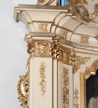 Zdjęcie nr 5: Ołtarz architektoniczny, jednokondygnacyjny, jednoosiowy ze zwieńczeniem. Ołtarz prostopadłościenny, z drewnianą mensą, z antepedium ujętym po bokach parą konsoli w formie wolut. Pole antepedium w postaci prostokątnej płyciny z płaskorzeźbionym motywem gorejącego serca pośrodku, ujętego promienistą glorią. Na mensie tabernakulum w formie prostopadłościennej szafki o wypukłej, przedniej  ściance ujętej dwoma parami osadzonych na niewielkich cokołach kolumienek wspierających niepełne, wyłamujące się ponad nimi belkowanie. Drzwiczki w kształcie stojącego prostokąta zamkniętego półkolistym łukiem nadwieszonym, zdobione motywem płaskorzeźbionego kielicha eucharystycznego. Struktura zdobiona motywami rozet i wici roślinnej. Retabulum osadzone na niewysokim, zryzalitowanym po bokach cokole. Część środkową nastawy ujmuje para ustawionych skośnie  filarów wspierających wyłamujące się ponad nimi belkowanie. Zamknięte półkoliście zwieńczenie ujmuje para spływów wolutowych oraz flankuje przerwany, wolutowy przyczółek. Pola wolutowych konsoli zdobi para liści akantu, cokół retabulum para stylizowanych słoneczników i S-kształtnych wici. Zewnętrzne pola trzonów filarów zdobią w górnych partiach ukwiecone gałązki, wewnętrzne motyw podwieszeń skomponowanych z zamkniętej korony, krzyżujących się rogów obfitości i krzyża z kotwicą, oraz kokard, u dołu para gałązek. Boki pola środkowego z motywem wici winnego grona, u góry w narożach para ulistnionych rozet. Fryz zdobiony rozetami, pośrodku kartusz w monogramem imienia Jezus ujętym parą gałązek laurowych. Retabulum flankowane parą ażurowych uszaków rocaille’owych. W dolnej partii zwieńczenia uskrzydlona główka anielska, szczyt w formie konchy ujętej po bokach parą rocaille’i. Na przerwanym przyczółku para figur aniołków. Pole części środkowej w kształcie stojącego prostokąta zamkniętego półkolistym łukiem nadwieszonym z uskokami, ujęte profilowaną, złoconą ramą, w środku wizerunek Najświętszego Serca Jezusa. Po bokach, na tle filarów para figur, po lewej św. Szczepan, po prawej św. Wawrzyniec. W zwieńczeniu obraz w kształcie trapezu o wklęsłych ramionach, podstawie i dolnych narożach, zamknięty półkolistym łukiem nadwieszonym, ujęty profilowaną, złoconą ramą, z wizerunkiem św. Katarzyny Aleksandryjskiej. 
Struktura w kolorze kremowym, detal architektoniczny i ornamentyka złocone.    
