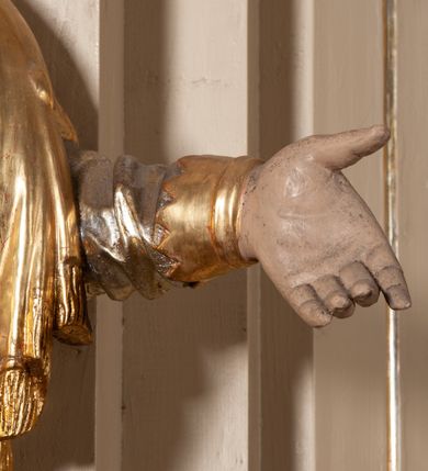 Zdjęcie nr 9: Całopostaciowa, pełnoplastyczna figura św. Szczepana stojącego w lekkim kontrapoście na niewysokiej podstawie, zwróconego w trzech czwartych w lewo. Podniesioną głowę charakteryzuje owalna twarz o młodzieńczych  rysach z niskim czołem, wysoko uniesionymi brwiami, dużymi oczami długim nosem i kształtnymi ustami w lekkim uśmiechu. Włosy krótkie, sięgające szyi, z krótką grzywką, odsłaniające uszy. Święty ubrany w srebrzoną, silnie fałdowaną albę obszytą ząbkowaną lamówką oraz złoconą, obszytą frędzlą dalmatykę z motywem korony z parą gałązek na piersiach oraz parą grubych sznurów zakończonych chwostami. Na nogach czarne buty. Lewa, zgięta w łokciu ręka wyciągnięta przed siebie z dłonią skierowaną w dół, prawą podtrzymuje kamień i gałązkę palmową.       