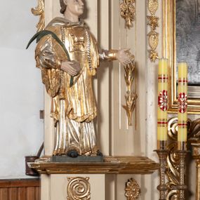 Zdjęcie nr 1: Całopostaciowa, pełnoplastyczna figura św. Szczepana stojącego w lekkim kontrapoście na niewysokiej podstawie, zwróconego w trzech czwartych w lewo. Podniesioną głowę charakteryzuje owalna twarz o młodzieńczych  rysach z niskim czołem, wysoko uniesionymi brwiami, dużymi oczami długim nosem i kształtnymi ustami w lekkim uśmiechu. Włosy krótkie, sięgające szyi, z krótką grzywką, odsłaniające uszy. Święty ubrany w srebrzoną, silnie fałdowaną albę obszytą ząbkowaną lamówką oraz złoconą, obszytą frędzlą dalmatykę z motywem korony z parą gałązek na piersiach oraz parą grubych sznurów zakończonych chwostami. Na nogach czarne buty. Lewa, zgięta w łokciu ręka wyciągnięta przed siebie z dłonią skierowaną w dół, prawą podtrzymuje kamień i gałązkę palmową.       