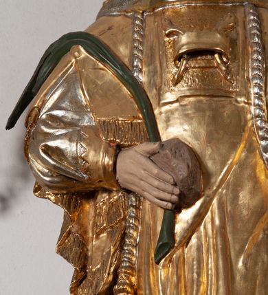 Zdjęcie nr 5: Całopostaciowa, pełnoplastyczna figura św. Szczepana stojącego w lekkim kontrapoście na niewysokiej podstawie, zwróconego w trzech czwartych w lewo. Podniesioną głowę charakteryzuje owalna twarz o młodzieńczych  rysach z niskim czołem, wysoko uniesionymi brwiami, dużymi oczami długim nosem i kształtnymi ustami w lekkim uśmiechu. Włosy krótkie, sięgające szyi, z krótką grzywką, odsłaniające uszy. Święty ubrany w srebrzoną, silnie fałdowaną albę obszytą ząbkowaną lamówką oraz złoconą, obszytą frędzlą dalmatykę z motywem korony z parą gałązek na piersiach oraz parą grubych sznurów zakończonych chwostami. Na nogach czarne buty. Lewa, zgięta w łokciu ręka wyciągnięta przed siebie z dłonią skierowaną w dół, prawą podtrzymuje kamień i gałązkę palmową.       