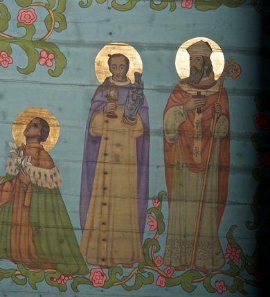 Zdjęcie nr 22: Ściany kościoła dekorują przedstawienia świętych: św. Stanisław w stroju pontyfikalnym z pastorałem, wskrzeszający Piotrowina. Poniżej na banderoli napis „BŁOGOSŁAWIENI KTÓRZY ŁAKNĄ / I PRAGNĄ SPRAWIEDLIWOŚCI”; św. Jadwiga w koronie i płaszczu podszytym gronostajem, trzymająca skrzyneczkę z klejnotami oraz krzyż z herbami Polski i Litwy. Na banderoli napis „BŁOGOSŁAWIENI / POKÓJ CZYNIĄCY”; św. Jan Kanty błogosławiący dziewczynę z dzbanem podpisany „BŁOGOSŁAWIENI / MIŁOSIERNI”; św. w habicie, z krzyżem w ręce i w asyście dwóch aniołów - jednego z palmą męczeństwa, drugiego z płonącą pochodnią, pod nimi napis „BŁOGOSŁAWIENI KTÓRZY / CIERPIĄ PRZEŚLADOWANIA DLA SPRAWIEDLIWOŚCI”; Chrystus z sercem gorejącym. Po jego prawej stronie klęczący mężczyzna, po lewej dwie owieczki nad strumieniem. Scena podpisana: „KTÓRZY PRACUJECIE I / OBCIĄŻENI JESTEŚCIE / A JA WAS OCHŁODZĘ”; archanioł Gabriel z lilią powyżej napisu  „ZDROWAŚ MARIO”; archanioł Michał z trybularzem, ponad napisem „KTÓŻ JAK BÓG!”; św. Franciszek na tle przyrody. Jest ubrany w habit franciszkański, na głowie ma kaptur. Przy prawej nodze świętego wilk, w jeziorze ryby, na niebie ptaki. Na banderoli napis „BŁOGOSŁAWIENI UBODZY DUCHEM / ALBOWIEM TAKOWYCH JEST / KRÓLESTWO NIEBIESKIE”; św. Izydor Oracz ukazany w towarzystwie anioła orającego na polu na tle dzwonnicy. Poniżej napis „BŁOGOSŁAWIENI CISI / ALBOWIEM ONI / POSIĄDĄ ZIEMIĘ”. Poniżej postaci świętych fryz z przedstawieniem 14 stacji drogi krzyżowej na błękitnym tle. Na stropie nawy i prezbiterium, na błękitnym tle, wśród kwiatowego ornamentu na środku ukazany Chrystus Ukrzyżowany ponad kielichem, gołębica Ducha Świętego i koronowana Maria. Po ich obu stronach stoją święci mężowie i niewiasty z atrybutami. W nawie w kolejności do środka: św. Wojciech (?), św. Jacek z figurą Matki Boskiej i monstrancją, klęczący św. Kazimierz w stroju książęcym z lilią, św. Agnieszka z barankiem i św. Karolina Kózkówna z różańcem, klęcząca św. Rozalia z różami, św. Klara z cyborium, św. Weronika z chustą z wizerunkiem Chrystusa, klęcząca św. Cecylia z lirą, św. Józef z lilią, św. Paweł z mieczem, klęczący św. Jan Chrzciciel z krzyżem. W prezbiterium przedstawiono 12 apostołów, niektórzy z atrybutmi, które ich jednoznacznie identyfilują, np. św. Andrzej z krzyżem w kształcie litery X, inni z księgami lub zwojami.  