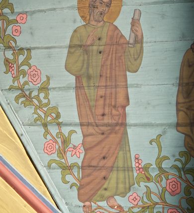 Zdjęcie nr 29: Ściany kościoła dekorują przedstawienia świętych: św. Stanisław w stroju pontyfikalnym z pastorałem, wskrzeszający Piotrowina. Poniżej na banderoli napis „BŁOGOSŁAWIENI KTÓRZY ŁAKNĄ / I PRAGNĄ SPRAWIEDLIWOŚCI”; św. Jadwiga w koronie i płaszczu podszytym gronostajem, trzymająca skrzyneczkę z klejnotami oraz krzyż z herbami Polski i Litwy. Na banderoli napis „BŁOGOSŁAWIENI / POKÓJ CZYNIĄCY”; św. Jan Kanty błogosławiący dziewczynę z dzbanem podpisany „BŁOGOSŁAWIENI / MIŁOSIERNI”; św. w habicie, z krzyżem w ręce i w asyście dwóch aniołów - jednego z palmą męczeństwa, drugiego z płonącą pochodnią, pod nimi napis „BŁOGOSŁAWIENI KTÓRZY / CIERPIĄ PRZEŚLADOWANIA DLA SPRAWIEDLIWOŚCI”; Chrystus z sercem gorejącym. Po jego prawej stronie klęczący mężczyzna, po lewej dwie owieczki nad strumieniem. Scena podpisana: „KTÓRZY PRACUJECIE I / OBCIĄŻENI JESTEŚCIE / A JA WAS OCHŁODZĘ”; archanioł Gabriel z lilią powyżej napisu  „ZDROWAŚ MARIO”; archanioł Michał z trybularzem, ponad napisem „KTÓŻ JAK BÓG!”; św. Franciszek na tle przyrody. Jest ubrany w habit franciszkański, na głowie ma kaptur. Przy prawej nodze świętego wilk, w jeziorze ryby, na niebie ptaki. Na banderoli napis „BŁOGOSŁAWIENI UBODZY DUCHEM / ALBOWIEM TAKOWYCH JEST / KRÓLESTWO NIEBIESKIE”; św. Izydor Oracz ukazany w towarzystwie anioła orającego na polu na tle dzwonnicy. Poniżej napis „BŁOGOSŁAWIENI CISI / ALBOWIEM ONI / POSIĄDĄ ZIEMIĘ”. Poniżej postaci świętych fryz z przedstawieniem 14 stacji drogi krzyżowej na błękitnym tle. Na stropie nawy i prezbiterium, na błękitnym tle, wśród kwiatowego ornamentu na środku ukazany Chrystus Ukrzyżowany ponad kielichem, gołębica Ducha Świętego i koronowana Maria. Po ich obu stronach stoją święci mężowie i niewiasty z atrybutami. W nawie w kolejności do środka: św. Wojciech (?), św. Jacek z figurą Matki Boskiej i monstrancją, klęczący św. Kazimierz w stroju książęcym z lilią, św. Agnieszka z barankiem i św. Karolina Kózkówna z różańcem, klęcząca św. Rozalia z różami, św. Klara z cyborium, św. Weronika z chustą z wizerunkiem Chrystusa, klęcząca św. Cecylia z lirą, św. Józef z lilią, św. Paweł z mieczem, klęczący św. Jan Chrzciciel z krzyżem. W prezbiterium przedstawiono 12 apostołów, niektórzy z atrybutmi, które ich jednoznacznie identyfilują, np. św. Andrzej z krzyżem w kształcie litery X, inni z księgami lub zwojami.  