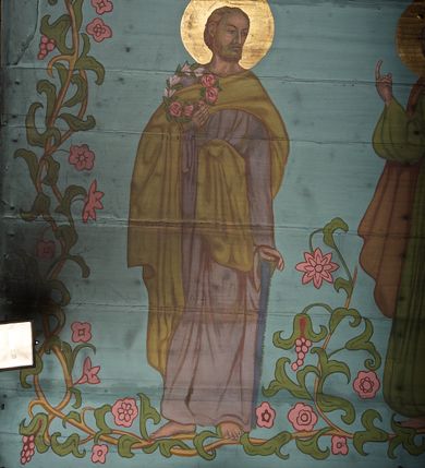 Zdjęcie nr 37: Ściany kościoła dekorują przedstawienia świętych: św. Stanisław w stroju pontyfikalnym z pastorałem, wskrzeszający Piotrowina. Poniżej na banderoli napis „BŁOGOSŁAWIENI KTÓRZY ŁAKNĄ / I PRAGNĄ SPRAWIEDLIWOŚCI”; św. Jadwiga w koronie i płaszczu podszytym gronostajem, trzymająca skrzyneczkę z klejnotami oraz krzyż z herbami Polski i Litwy. Na banderoli napis „BŁOGOSŁAWIENI / POKÓJ CZYNIĄCY”; św. Jan Kanty błogosławiący dziewczynę z dzbanem podpisany „BŁOGOSŁAWIENI / MIŁOSIERNI”; św. w habicie, z krzyżem w ręce i w asyście dwóch aniołów - jednego z palmą męczeństwa, drugiego z płonącą pochodnią, pod nimi napis „BŁOGOSŁAWIENI KTÓRZY / CIERPIĄ PRZEŚLADOWANIA DLA SPRAWIEDLIWOŚCI”; Chrystus z sercem gorejącym. Po jego prawej stronie klęczący mężczyzna, po lewej dwie owieczki nad strumieniem. Scena podpisana: „KTÓRZY PRACUJECIE I / OBCIĄŻENI JESTEŚCIE / A JA WAS OCHŁODZĘ”; archanioł Gabriel z lilią powyżej napisu  „ZDROWAŚ MARIO”; archanioł Michał z trybularzem, ponad napisem „KTÓŻ JAK BÓG!”; św. Franciszek na tle przyrody. Jest ubrany w habit franciszkański, na głowie ma kaptur. Przy prawej nodze świętego wilk, w jeziorze ryby, na niebie ptaki. Na banderoli napis „BŁOGOSŁAWIENI UBODZY DUCHEM / ALBOWIEM TAKOWYCH JEST / KRÓLESTWO NIEBIESKIE”; św. Izydor Oracz ukazany w towarzystwie anioła orającego na polu na tle dzwonnicy. Poniżej napis „BŁOGOSŁAWIENI CISI / ALBOWIEM ONI / POSIĄDĄ ZIEMIĘ”. Poniżej postaci świętych fryz z przedstawieniem 14 stacji drogi krzyżowej na błękitnym tle. Na stropie nawy i prezbiterium, na błękitnym tle, wśród kwiatowego ornamentu na środku ukazany Chrystus Ukrzyżowany ponad kielichem, gołębica Ducha Świętego i koronowana Maria. Po ich obu stronach stoją święci mężowie i niewiasty z atrybutami. W nawie w kolejności do środka: św. Wojciech (?), św. Jacek z figurą Matki Boskiej i monstrancją, klęczący św. Kazimierz w stroju książęcym z lilią, św. Agnieszka z barankiem i św. Karolina Kózkówna z różańcem, klęcząca św. Rozalia z różami, św. Klara z cyborium, św. Weronika z chustą z wizerunkiem Chrystusa, klęcząca św. Cecylia z lirą, św. Józef z lilią, św. Paweł z mieczem, klęczący św. Jan Chrzciciel z krzyżem. W prezbiterium przedstawiono 12 apostołów, niektórzy z atrybutmi, które ich jednoznacznie identyfilują, np. św. Andrzej z krzyżem w kształcie litery X, inni z księgami lub zwojami.  