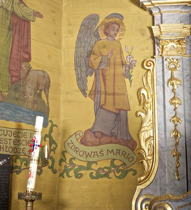 Zdjęcie nr 38: Ściany kościoła dekorują przedstawienia świętych: św. Stanisław w stroju pontyfikalnym z pastorałem, wskrzeszający Piotrowina. Poniżej na banderoli napis „BŁOGOSŁAWIENI KTÓRZY ŁAKNĄ / I PRAGNĄ SPRAWIEDLIWOŚCI”; św. Jadwiga w koronie i płaszczu podszytym gronostajem, trzymająca skrzyneczkę z klejnotami oraz krzyż z herbami Polski i Litwy. Na banderoli napis „BŁOGOSŁAWIENI / POKÓJ CZYNIĄCY”; św. Jan Kanty błogosławiący dziewczynę z dzbanem podpisany „BŁOGOSŁAWIENI / MIŁOSIERNI”; św. w habicie, z krzyżem w ręce i w asyście dwóch aniołów - jednego z palmą męczeństwa, drugiego z płonącą pochodnią, pod nimi napis „BŁOGOSŁAWIENI KTÓRZY / CIERPIĄ PRZEŚLADOWANIA DLA SPRAWIEDLIWOŚCI”; Chrystus z sercem gorejącym. Po jego prawej stronie klęczący mężczyzna, po lewej dwie owieczki nad strumieniem. Scena podpisana: „KTÓRZY PRACUJECIE I / OBCIĄŻENI JESTEŚCIE / A JA WAS OCHŁODZĘ”; archanioł Gabriel z lilią powyżej napisu  „ZDROWAŚ MARIO”; archanioł Michał z trybularzem, ponad napisem „KTÓŻ JAK BÓG!”; św. Franciszek na tle przyrody. Jest ubrany w habit franciszkański, na głowie ma kaptur. Przy prawej nodze świętego wilk, w jeziorze ryby, na niebie ptaki. Na banderoli napis „BŁOGOSŁAWIENI UBODZY DUCHEM / ALBOWIEM TAKOWYCH JEST / KRÓLESTWO NIEBIESKIE”; św. Izydor Oracz ukazany w towarzystwie anioła orającego na polu na tle dzwonnicy. Poniżej napis „BŁOGOSŁAWIENI CISI / ALBOWIEM ONI / POSIĄDĄ ZIEMIĘ”. Poniżej postaci świętych fryz z przedstawieniem 14 stacji drogi krzyżowej na błękitnym tle. Na stropie nawy i prezbiterium, na błękitnym tle, wśród kwiatowego ornamentu na środku ukazany Chrystus Ukrzyżowany ponad kielichem, gołębica Ducha Świętego i koronowana Maria. Po ich obu stronach stoją święci mężowie i niewiasty z atrybutami. W nawie w kolejności do środka: św. Wojciech (?), św. Jacek z figurą Matki Boskiej i monstrancją, klęczący św. Kazimierz w stroju książęcym z lilią, św. Agnieszka z barankiem i św. Karolina Kózkówna z różańcem, klęcząca św. Rozalia z różami, św. Klara z cyborium, św. Weronika z chustą z wizerunkiem Chrystusa, klęcząca św. Cecylia z lirą, św. Józef z lilią, św. Paweł z mieczem, klęczący św. Jan Chrzciciel z krzyżem. W prezbiterium przedstawiono 12 apostołów, niektórzy z atrybutmi, które ich jednoznacznie identyfilują, np. św. Andrzej z krzyżem w kształcie litery X, inni z księgami lub zwojami.  