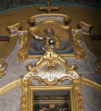 Zdjęcie nr 9: Ołtarz architektoniczny, jednoosiowy, jednokondygnacyjny. Mensa prostopadłościenna z antepedium haftowanym bogatą dekoracją kwiatową, z centralnie umieszczonym kielichem w otoczeniu winnej latorośli. Na nim tabernakulum w formie zbliżonej do prostopadłościennej skrzynki o wypukłej ściance frontowej na tle ścianki z tronem wystawienia ustawionej na cokole i ujętej spływami wolutowymi. Drzwiczki tabernakulum dekorowane krzyżem z glorią między literami „Α” i „Ω”. Tron wystawienia złocony, dekorowany kwiatem między stylizowanymi liśćmi i ujęty od góry muszlą palmetową. Tron ujmują lizeny przedzielone i zwieńczone gzymsem ustawionym skośnie i zakończonym od wewnętrznej strony wolutami. Gzyms nad tronem wystawienia wyniesiony, w formie łuku nadwieszonego. Na jego zewnętrznych częściach posadowiono figurki klęczących i modlących się aniołków. Nastawa ujęta parą zdwojonych pilastrów na cokołach, o głowicach korynckich, z impostami z dekoracją w formie festonów z rocaille’em i liśćmi. Uszy w formie spływów wolutowych z dekoracją liściastą. W centrum pole obrazowe z wnęką o profilowanej ramie w kształcie stojącego prostokąta ujętego w spływy wolutowe i festony, zwieńczone wydatnym kartuszem dekorowanym rocaille’em, z monogramem maryjnym. W nim ukazana Matka Boska Anielska przesłaniana obrazem „Wszyscy Święci” wzorowanym na obrazie Rafaela. Retabulum przedzielone gzymsem wyniesionym w łuk ponad polem centralnym. Zwieńczenie w formie zbliżonej do prostokąta, rozszerzające się ku dołowi, ujęte w esowate pilastry przechodzące w woluty, zamknięte łukiem odcinkowym zakończonym wolutami. Całość wieńczy krzyż z rozetą na skrzyżowaniu ramion. W zwieńczeniu wklęsło-wypukłe pole obrazowe z płaskorzeźbionym popiersiem Boga Ojca na tle nieba. Na impostach leżące figury aniołów. Struktura polichromowana, marmoryzowana w odcieniu jasnoszarym, profile, ornamenty i dekoracje złocone i srebrzone. 