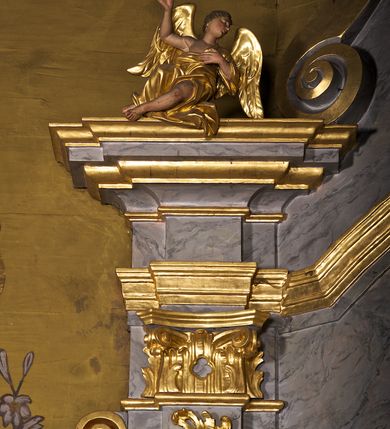 Zdjęcie nr 5: Ołtarz architektoniczny, jednoosiowy, jednokondygnacyjny. Mensa prostopadłościenna z antepedium haftowanym bogatą dekoracją kwiatową, z centralnie umieszczonym kielichem w otoczeniu winnej latorośli. Na nim tabernakulum w formie zbliżonej do prostopadłościennej skrzynki o wypukłej ściance frontowej na tle ścianki z tronem wystawienia ustawionej na cokole i ujętej spływami wolutowymi. Drzwiczki tabernakulum dekorowane krzyżem z glorią między literami „Α” i „Ω”. Tron wystawienia złocony, dekorowany kwiatem między stylizowanymi liśćmi i ujęty od góry muszlą palmetową. Tron ujmują lizeny przedzielone i zwieńczone gzymsem ustawionym skośnie i zakończonym od wewnętrznej strony wolutami. Gzyms nad tronem wystawienia wyniesiony, w formie łuku nadwieszonego. Na jego zewnętrznych częściach posadowiono figurki klęczących i modlących się aniołków. Nastawa ujęta parą zdwojonych pilastrów na cokołach, o głowicach korynckich, z impostami z dekoracją w formie festonów z rocaille’em i liśćmi. Uszy w formie spływów wolutowych z dekoracją liściastą. W centrum pole obrazowe z wnęką o profilowanej ramie w kształcie stojącego prostokąta ujętego w spływy wolutowe i festony, zwieńczone wydatnym kartuszem dekorowanym rocaille’em, z monogramem maryjnym. W nim ukazana Matka Boska Anielska przesłaniana obrazem „Wszyscy Święci” wzorowanym na obrazie Rafaela. Retabulum przedzielone gzymsem wyniesionym w łuk ponad polem centralnym. Zwieńczenie w formie zbliżonej do prostokąta, rozszerzające się ku dołowi, ujęte w esowate pilastry przechodzące w woluty, zamknięte łukiem odcinkowym zakończonym wolutami. Całość wieńczy krzyż z rozetą na skrzyżowaniu ramion. W zwieńczeniu wklęsło-wypukłe pole obrazowe z płaskorzeźbionym popiersiem Boga Ojca na tle nieba. Na impostach leżące figury aniołów. Struktura polichromowana, marmoryzowana w odcieniu jasnoszarym, profile, ornamenty i dekoracje złocone i srebrzone. 