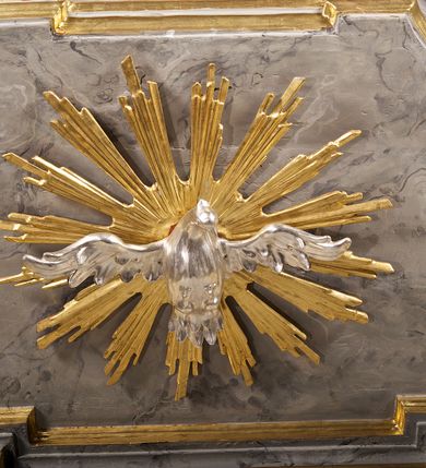 Zdjęcie nr 6: Ambona przyścienna składająca się z kosza, zaplecka i baldachimu zawieszona na lewej ścianie prezbiterium. Kosz na planie kwadratu, o wklęsłych narożach dekorowanych rocaille'em i ujętych pilastrami, dekorowany ramami o krótkich krawędziach utworzonych z ornamentu rocaille’owego; parapet profilowany, wklęsło-wypukły. Podstawę tworzy stylizowany motyw muszli, z podwieszonym ośmiobokiem zakończonym kwiatonem. Zaplecek gładki, zamknięty belkowaniem, podtrzymany na konsolach, z których zwiesza się ornament roślinny. W dolnej części płycina w kształcie leżącego prostokąta. Baldachim powtarzający kształt kosza, w formie bogato profilowanego gzymsu z gołębicą w glorii na podniebieniu. Powyżej gzymsu baldachim przechodzi w zwężający się, dekolorowany rocaille'em cokół, na którym znajduje się pełnoplastyczna rzeźba anioła siedzącego na chmurze, dmącego w trąbę trzymaną w prawej ręce, lewą ujmującego płomienisty miecz. Anioł ukazany został w skręcie w prawo, z głową lekko uniesioną i rozłożonymi skrzydłami. Jest ubrany w obszerny, złoty płaszcz, spod którego wystaje prawa noga. Struktura marmoryzowana na kolor jasnoszary; ornamenty, profile i fragmenty rzeźb złocone, gołębica, chmura i trąba srebrzone. 