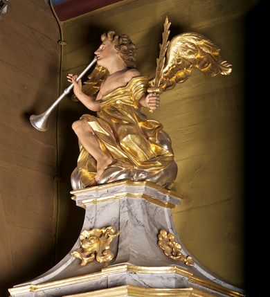 Zdjęcie nr 5: Ambona przyścienna składająca się z kosza, zaplecka i baldachimu zawieszona na lewej ścianie prezbiterium. Kosz na planie kwadratu, o wklęsłych narożach dekorowanych rocaille'em i ujętych pilastrami, dekorowany ramami o krótkich krawędziach utworzonych z ornamentu rocaille’owego; parapet profilowany, wklęsło-wypukły. Podstawę tworzy stylizowany motyw muszli, z podwieszonym ośmiobokiem zakończonym kwiatonem. Zaplecek gładki, zamknięty belkowaniem, podtrzymany na konsolach, z których zwiesza się ornament roślinny. W dolnej części płycina w kształcie leżącego prostokąta. Baldachim powtarzający kształt kosza, w formie bogato profilowanego gzymsu z gołębicą w glorii na podniebieniu. Powyżej gzymsu baldachim przechodzi w zwężający się, dekolorowany rocaille'em cokół, na którym znajduje się pełnoplastyczna rzeźba anioła siedzącego na chmurze, dmącego w trąbę trzymaną w prawej ręce, lewą ujmującego płomienisty miecz. Anioł ukazany został w skręcie w prawo, z głową lekko uniesioną i rozłożonymi skrzydłami. Jest ubrany w obszerny, złoty płaszcz, spod którego wystaje prawa noga. Struktura marmoryzowana na kolor jasnoszary; ornamenty, profile i fragmenty rzeźb złocone, gołębica, chmura i trąba srebrzone. 