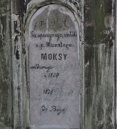 Zdjęcie nr 1: Nagrobek kamienny na cokole, w formie prostopadłościanu o fazowanych bokach, zakończony wyniesionym, uproszczonym trójkątnym przyczółkiem. W zwieńczeniu owalny medalion, w którym mógł znajdować się wizerunek Chrystusa, obecnie bardzo zniszczony, ujęty wieńcem (?). Poniżej płycina zamknięta łukiem półkolistym i inskrypcją „D(EO) O(PTIMO) M(AXIMO) / Tu spoczywają zwłoki / s(więtej) p(amięci) Wicentego / MOKSY / urodzonego [...] / * 1800 [...] / [...] 1870 [...] / [...] do Boga”. Powyżej płyciny rzeźbiona głowa w owalnym medalionie. Nagrobek był ziweńczony krzyżem, obecnie ułamanym, leżącym obok cokołu. Na przedniej ścianie, na cokole sygnatura kamieniarza F. HOCHSTIM.