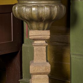 Zdjęcie nr 1: Stopa chrzcielnicy jest profilowana, ośmioboczna zakończona takimż pierścieniem. Trzon kwadratowy, profilowany, wklęsłowypukły. Misa jest puklowana, wklęsłowypukła, kolista z wywiniętym brzegiem. Na niej pokrywa w formie sześciu schodzących się koncentrycznie wolut dekorowanych ornamentem roślinnym, podtrzymujących profilowany talerzyk. Zwieńczenie w formie rzeźby Matki Boskiej z Fatimy na prostopadłościennej, dwustrefowej podstawie. Maria została ukazana w całej postaci, stojąca na chmurach, z rękami złożonymi do modlitwy i głową delikatnie przechyloną na lewo. Jej owalna twarz zakończona spiczastym podbródkiem ma pogodny wyraz. Maria ma na sobie białą suknię ze złotymi lamowaniami i obszerny, jasnoróżowy maforion; na głowie niewielką, zamkniętą koronę. 
Stopa i trzon w kolorze piaskowca, czara szara. 