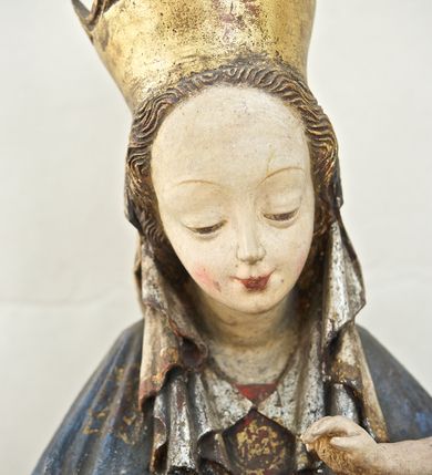 Zdjęcie nr 3: Rzeźba pełna, ukazująca Matkę Boską z Dzieciątkiem na niskiej, wielobocznej podstawie. Maria stoi, lewą ręką podtrzymuje Jezusa, a prawą podaje mu jabłko i spogląda na ten gest. Ma owalną, pełną twarz, o wysokim czole, wąskich brwiach, dużych, półprzymkniętych oczach, niewielkim nosie i ustach rozchylonych w delikatnym uśmiechu. Jest ubrana w czerwoną suknię ze złotym ornamentem, której fragment widać przy prawej nodze i bardzo obszerny, gęsto drapowany granatowy płaszcz ze złotym ornamentem i srebrnym podbiciem. Wierzchnie okrycie owija się wokół lewej ręki Madonny i szerokimi, twardo giętymi fałdami spływa w dół; przy prawym biodrze tworzy rurkowato zwinięte kaskady. Maria ma na głowę zarzucony welon, który, wywijając się, spływa na dekolt oraz wysoką, złotą, otwarta koronę. Rzeźba jest sygnowana z tyłu przy dolnej krawędzi „A(NDRZEJ) WALIJEWSKI”. Polichromia w partiach ciała naturalistyczna. 