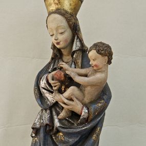 Zdjęcie nr 1: Rzeźba pełna, ukazująca Matkę Boską z Dzieciątkiem na niskiej, wielobocznej podstawie. Maria stoi, lewą ręką podtrzymuje Jezusa, a prawą podaje mu jabłko i spogląda na ten gest. Ma owalną, pełną twarz, o wysokim czole, wąskich brwiach, dużych, półprzymkniętych oczach, niewielkim nosie i ustach rozchylonych w delikatnym uśmiechu. Jest ubrana w czerwoną suknię ze złotym ornamentem, której fragment widać przy prawej nodze i bardzo obszerny, gęsto drapowany granatowy płaszcz ze złotym ornamentem i srebrnym podbiciem. Wierzchnie okrycie owija się wokół lewej ręki Madonny i szerokimi, twardo giętymi fałdami spływa w dół; przy prawym biodrze tworzy rurkowato zwinięte kaskady. Maria ma na głowę zarzucony welon, który, wywijając się, spływa na dekolt oraz wysoką, złotą, otwarta koronę. Rzeźba jest sygnowana z tyłu przy dolnej krawędzi „A(NDRZEJ) WALIJEWSKI”. Polichromia w partiach ciała naturalistyczna. 