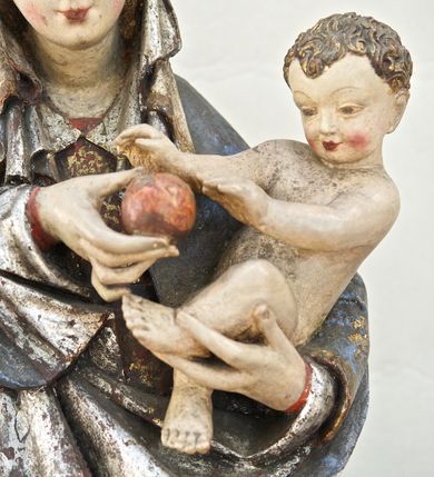 Zdjęcie nr 2: Rzeźba pełna, ukazująca Matkę Boską z Dzieciątkiem na niskiej, wielobocznej podstawie. Maria stoi, lewą ręką podtrzymuje Jezusa, a prawą podaje mu jabłko i spogląda na ten gest. Ma owalną, pełną twarz, o wysokim czole, wąskich brwiach, dużych, półprzymkniętych oczach, niewielkim nosie i ustach rozchylonych w delikatnym uśmiechu. Jest ubrana w czerwoną suknię ze złotym ornamentem, której fragment widać przy prawej nodze i bardzo obszerny, gęsto drapowany granatowy płaszcz ze złotym ornamentem i srebrnym podbiciem. Wierzchnie okrycie owija się wokół lewej ręki Madonny i szerokimi, twardo giętymi fałdami spływa w dół; przy prawym biodrze tworzy rurkowato zwinięte kaskady. Maria ma na głowę zarzucony welon, który, wywijając się, spływa na dekolt oraz wysoką, złotą, otwarta koronę. Rzeźba jest sygnowana z tyłu przy dolnej krawędzi „A(NDRZEJ) WALIJEWSKI”. Polichromia w partiach ciała naturalistyczna. 