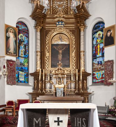 Zdjęcie nr 11: Ołtarz przyścienny, architektoniczny, jednoosiowy, jednokondygnacyjny ze zwieńczeniem. Mensa drewniana w kształcie prostopadłościennej skrzyni z narożami lekko wysuniętymi przed jej lico. Antependium drewniane z umieszczoną w centrum prostokątną płyciną z płaskorzeźbioną sceną Ostatniej Wieczerzy według Leonarda da Vinci. Po bokach po dwie mniejsze płyciny w kształcie prostokąta stojącego wypełnione płaskorzeźbioną, złoconą dekoracją z winnym gronem, kłosami, kwiatami oraz muszlą palmetową. 
Tabernakulum w kształcie prostopadłościennej, obitej metalową blachą skrzynki, dwudrzwiowe. Na drzwiczkach odlewana dekoracja z kłosów i winnych gron, powyżej gorejące serce. Tabernakulum ujęte drewnianym tronem wystawienia w formie ażurowej kolumnady na planie półkola. Zwieńczone ażurowymi wolutami tworzącymi formę baldachimu. U szczytu korona zamknięta, u jej podstawy Baranek Apokaliptyczny. 
Retabulum ustawione na wysokim cokole z bokami zwróconymi pod kątem 45 stopni, zwieńczonym wydatnym profilowanym gzymsem. Na ścianach cokołów uskrzydlone główki aniołów z podwieszonym ornamentem o motywach cęgowych i roślinnych. Kondygnacja flankowana jest parą kolumn podtrzymujących niepełne belkowanie. Kolumny o kapitelach kompozytowych, marmoryzowanych trzonach, z nałożoną do połowy dekoracją w formie ornamentalnej wici roślinnej złożonej z motywów akantu, rocaille&#039;u, palmety i ornamentu cęgowego. Na gzymsie fragmenty przerwanego trójkątnego przyczółka, na których siedzą pełnoplastyczne figury aniołków. Pole główne ołtarza o lekko zaoblonych narożach, w jego centrum złocona, profilowana rama w otoku z cierniowej korony, o kształcie prostokąta stojącego zakończonego półkoliście. Pośrodku obraz Matki Boskiej Częstochowskiej oraz obraz Ukrzyżowanie na zasuwie, ponad którym umieszczona jest płaskorzeźba Boga Ojca. Powyżej, na osi ołtarza złocona korona z krzyżykiem. 
Zwieńczenie ujęte jest kolumnami analogicznymi jak w kondygnacji dźwigającymi niepełne, przełamane na osi podpór belkowanie o linii wklęsło-wypukłej. W polu promienista gloria z gołębicą Ducha Świętego na tle obłoków. Po bokach zwieńczenia znajdują się spływy wolutowe dekorowane kwiatami. U szczytu krzyż wyrastający z palmety. Ołtarz malowany na kolor brązowy, złocenia w partiach profili elementów architektonicznych i ornamentów złocone, detale srebrzone.