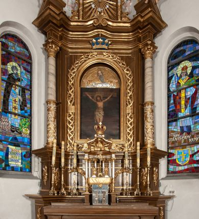 Zdjęcie nr 12: Ołtarz przyścienny, architektoniczny, jednoosiowy, jednokondygnacyjny ze zwieńczeniem. Mensa drewniana w kształcie prostopadłościennej skrzyni z narożami lekko wysuniętymi przed jej lico. Antependium drewniane z umieszczoną w centrum prostokątną płyciną z płaskorzeźbioną sceną Ostatniej Wieczerzy według Leonarda da Vinci. Po bokach po dwie mniejsze płyciny w kształcie prostokąta stojącego wypełnione płaskorzeźbioną, złoconą dekoracją z winnym gronem, kłosami, kwiatami oraz muszlą palmetową. 
Tabernakulum w kształcie prostopadłościennej, obitej metalową blachą skrzynki, dwudrzwiowe. Na drzwiczkach odlewana dekoracja z kłosów i winnych gron, powyżej gorejące serce. Tabernakulum ujęte drewnianym tronem wystawienia w formie ażurowej kolumnady na planie półkola. Zwieńczone ażurowymi wolutami tworzącymi formę baldachimu. U szczytu korona zamknięta, u jej podstawy Baranek Apokaliptyczny. 
Retabulum ustawione na wysokim cokole z bokami zwróconymi pod kątem 45 stopni, zwieńczonym wydatnym profilowanym gzymsem. Na ścianach cokołów uskrzydlone główki aniołów z podwieszonym ornamentem o motywach cęgowych i roślinnych. Kondygnacja flankowana jest parą kolumn podtrzymujących niepełne belkowanie. Kolumny o kapitelach kompozytowych, marmoryzowanych trzonach, z nałożoną do połowy dekoracją w formie ornamentalnej wici roślinnej złożonej z motywów akantu, rocaille'u, palmety i ornamentu cęgowego. Na gzymsie fragmenty przerwanego trójkątnego przyczółka, na których siedzą pełnoplastyczne figury aniołków. Pole główne ołtarza o lekko zaoblonych narożach, w jego centrum złocona, profilowana rama w otoku z cierniowej korony, o kształcie prostokąta stojącego zakończonego półkoliście. Pośrodku obraz Matki Boskiej Częstochowskiej oraz obraz Ukrzyżowanie na zasuwie, ponad którym umieszczona jest płaskorzeźba Boga Ojca. Powyżej, na osi ołtarza złocona korona z krzyżykiem. 
Zwieńczenie ujęte jest kolumnami analogicznymi jak w kondygnacji dźwigającymi niepełne, przełamane na osi podpór belkowanie o linii wklęsło-wypukłej. W polu promienista gloria z gołębicą Ducha Świętego na tle obłoków. Po bokach zwieńczenia znajdują się spływy wolutowe dekorowane kwiatami. U szczytu krzyż wyrastający z palmety. Ołtarz malowany na kolor brązowy, złocenia w partiach profili elementów architektonicznych i ornamentów złocone, detale srebrzone.