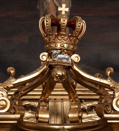 Zdjęcie nr 2: Tabernakulum dwudrzwiowe, w kształcie prostopadłościennej, obitej blachą metalową skrzynki. Na drzwiczkach odlewana dekoracja z kłosów i winnych gron, powyżej gorejące serce. Tabernakulum ujęte drewnianym tronem wystawienia w formie ażurowej kolumnady na planie półkola. Kolumny ustawione są na wysokich cokołach, wspierają niepełne belkowanie, zwieńczone sześcioma wolutami, spiętymi w kabłąk, tworzącymi formę połowy baldachimu. U szczytu korona zamknięta, pod nią Baranek Apokaliptyczny, a u spodu podwieszona szyszka otoczona liśćmi winogrona. Trzony kolumn w dolnej części zdobione są płaskorzeźbioną dekoracją roślinną, a w górnej części są gładkie, kapitele kompozytowe. Na tabernakulum ustawiona jest para adorujących aniołków, należących zapewne do kompletu tego zespołu. Aniołki ukazane są w pozycji klęczącej z rękami złożonymi w geście modlitwy i z pochylonymi głowami. Ubrane są w długie i złocone suknie.