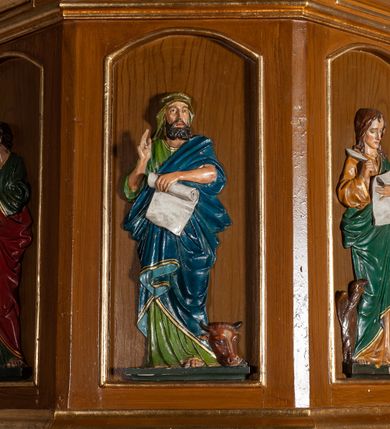 Zdjęcie nr 3: Ambona przyścienna, wisząca. Kosz ośmioboczny z silnie profilowaną podstawą, zakończony u dołu szyszką. Ścianki kosza zdobione pięcioma płycinami w formie stojących prostokątów, zamkniętych łukiem odcinkowym, z opaską malowaną na złoto. W każdej z czterech płycin płaskorzeźbione i polichromowane przedstawienie jednego z ewangelistów: Marka, Mateusza, Łukasza i Jana. Każda z postaci ukazana całopostaciowo, frontalnie, ze zwojem w lewej ręce, prawą czyniąca gest błogosławieństwa. U stóp ewangelistów przedstawiono odpowiadające im atrybuty: św. Marka – lew, św. Jana – orzeł, św. Mateusza – człowiek, św. Łukasza – wół. Balustrada ambony z belkowaniem, zdobionym motywem rautów we fryzie i kostkowaniem pod gzymsem. Ambona dostępna przez drewniane schody, od wschodu. Balustrada schodów zdobiona czterema romboidalnymi płycinami o brzegach malowanych na złoto. Struktura malowana w kolorze naturalnego drewna, detale i ornamentyka złocone.