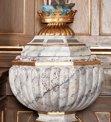 Zdjęcie nr 2: Chrzcielnica z pokrywą ustawiona na dwustopniowym, kamiennym cokole na rzucie kwadratu. Stopa w formie ośmiokąta foremnego na kształt jednolalkowej tralki, trzon żłobkowany. Czara ośmioboczna, puklowana. Pokrywa na ośmiobocznej, profilowanej podstawie z uszami po dwóch bokach, na bocznych i tylnych kwaterach napis „R(OKU) P(AŃSKIEGO) 1923 FUNDAT RZEPA z BUGAJU”.  Zwieńczona złoconą koroną, od dołu ujętą puklowaniem, na której ustawiona rzeźbiona, pełnoplastyczna scena Chrztu Chrystusa w Jordanie. Chrystus ukazany ze złożonymi rękami, stoi w wodzie, powyżej na skałach Jan Chrzciciel trzymający w lewej ręce wysoki krzyż, a w prawej konchę. Nad nimi wydłużona gloria z gołębicą Ducha Świętego. Tło sceny stanowi drzewo.