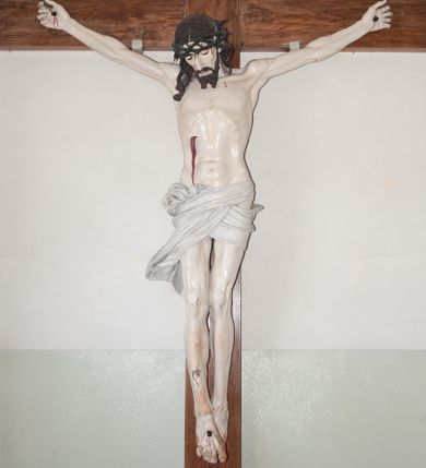 Zdjęcie nr 1: Chrystus ukazany w lekkim zwisie, o silnie zaznaczonej  anatomii, z wydatną klatką piersiową i zaznaczoną wyraźnie linią żeber. Nogi przybite do krzyża jednym gwoździem, założone prawa na lewą. Głowa lekko zwrócona w prawą stronę, skłoniona w dół. Twarz pociągła, nos prosty, oczy i usta lekko otwarte. Twarz okolona niewielkim zarostem ułożonym na końcu w dwa pukle; włosy długie, opadające na plecy i prawe ramię. Na głowie masywna korona cierniowa. Perizonium białe, ciasno oplatające biodra, z dłuższym końcem spływającym wzdłuż prawego uda. Nad głową Chrystusa prosty titulus z napisem „INRI”. Polichromia w odsłoniętych partiach ciała naturalistyczna. Krzyż gładki, ciemnobrązowy.
