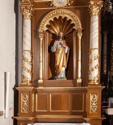 Zdjęcie nr 2: Pełnoplastyczna, polichromowana figura Chrystusa umieszczona w niszy ołtarza. Rzeźba ustawiona na niewielkim prostopadłościennym cokole o ściętych narożach. Chrystus przedstawiony całopostaciowo, w postawie stojącej z lekko ugiętym prawym kolanem, prawą ręką czyniący gest błogosławieństwa, lewą wskazujący na gorejące serce na piersi. Ubrany w długą, bladoniebieską suknię oraz złoty płaszcz przerzucony na lewe ramię i spływający pod prawą ręką. Twarz szczupła, owalna z migdałowymi oczami, długim i prostym nosem, wąskimi ustami. Włosy opadające na ramiona, krótki zarost. Na dłoniach widoczne ślady męki. 