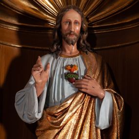 Zdjęcie nr 1: Pełnoplastyczna, polichromowana figura Chrystusa umieszczona w niszy ołtarza. Rzeźba ustawiona na niewielkim prostopadłościennym cokole o ściętych narożach. Chrystus przedstawiony całopostaciowo, w postawie stojącej z lekko ugiętym prawym kolanem, prawą ręką czyniący gest błogosławieństwa, lewą wskazujący na gorejące serce na piersi. Ubrany w długą, bladoniebieską suknię oraz złoty płaszcz przerzucony na lewe ramię i spływający pod prawą ręką. Twarz szczupła, owalna z migdałowymi oczami, długim i prostym nosem, wąskimi ustami. Włosy opadające na ramiona, krótki zarost. Na dłoniach widoczne ślady męki. 
