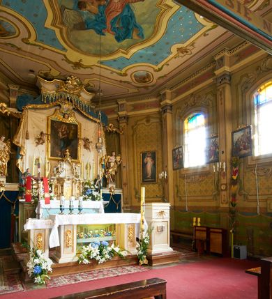 Zdjęcie nr 15: Polichromia ścian kościoła odpowiada podziałom architektonicznym wnętrza wydzielonym przez pilastry. Malowany zielony cokół w jednej czwartej wysokości ścian wyodrębniony jest pasem ornamentu geometrycznego, w nawie w jego polu znajdują się żółte prostokąty z dekoracją geometryczną, w prezbiterium malowana jasnozielona tkanina z dwoma pasami ornamentu roślinnego, medalionami z monogramami Marii i koronami oraz z motywem lilii heraldycznych i rozet. Trzony pilastrów wnętrza bladożółte z malowanymi płycinami dekorowanymi kampanulami, głowice zdobione malowanym kimationem. Na osi pilastrów, w partii fryzu, na tle niebieskich prostokątów uskrzydlone główki anielskie, pomiędzy nimi fryz wypełniony różowo-pomarańczowymi malowanymi płycinami w błękitnym obramieniu o fantazyjnym wykroju, dekorowanymi kampanulami. Belkowanie zamknięte malowanym pasem ornamentu geometrycznego. W polach pomiędzy pilastrami malowane płyciny o fantazyjnym kształcie zbliżonym do prostokąta, ujęte ramą zakończoną kartuszem, ich pola wypełnione są dekoracją geometryczną składającą się z krzyży równoramiennych w glorii i rozet wykonanych techniką patronową. Otwory okienne ujęte są malowanymi, imitującymi profilowanie obramieniami, otwory drzwiowe iluzjonistycznymi portalami z uszakami: portal w nawie zwieńczony jest kartuszem, a portal w prezbiterium zwieńczony jest szczytem zamkniętym fragmentem gzymsu w formie łuku segmentowego nadwieszonego podtrzymywanym przez spływy wolutowe. Pod chórem muzycznym malowane tablice pamiątkowe ujęte ramą, na ścianie północnej z napisem: „Ecclam hanc sub titulo Assumptionis B.V. Mariae a strenuo / milite Wierzbięta in Branice et Ruszcza Haerede pimo in / Wola juxta fines villae Stryjów a D. 1386 fundatam decimis / ex praedio Branice a colonis Stryjów, Wola, cuius sors est Grabie / Szczurów Zymbrzeg et ibidem taberna cum duobus pratis ac lacubus / Orzek et Piotrek ditatam, proper alluviem Vistulae  curatus suus / in hunc locum, qui erat pratum Gruczyn, ecclae dotale transtulit, / Hac tandem post annos 356 collapsa, quam vides, A.R.D. Jacobus Cichoński, parochus Grabiensis a.D. 1742 in loco desolatae  novam erexit. / Consecravit Illmus ac Rmus Michaël Kunicki, Sufraganeus Eppus. / Cracoviensis, Abbas Clarae Tumbae a D. 1749. / Restauravit A.R.D. Josephus Raźny, parochus Grabiensis a.D. 1907. / e colectis parochianorum.”; na ścianie południowej z napisem: „Ku Pamięci! / Dzieci Moje Najmilsze - Ja Prastara Świątynia / Polska dziękuję Wam za serdeczną troskę / o mnie. Oto dzięki Waszym ofiarom Drodzy / Rodzice i Twoim wysiłkom Kochana Młodzieży / w r. 1959 odnowiło się moje oblicze - rozjaśniały /  moje ołtarze, a w r. 1960 zabrzmiał mój nowy / organ na większą chwałę Bożą. Ja Was za to / rodzę na nowo do życia łaski. Ja Was błogosławię / na życie rodzinne. Ja Was prowadzę ku Bogu. Ja / Was także żegnam poraz ostatni, gdy przechodzicie / z tego padołu płaczu do wieczności, aby / Was znowu powitać kiedyś w niebie.”. Na ścianie zachodniej, pod chórem, nad środkowym otworem przejściowym pozostałości dawnego iluzjonistycznego portalu z kartuszem herbowym. Na stropie prezbiterium wydzielone pole o kształcie powtarzającym plan prezbiterium, wewnątrz pole w formie kwadratu o wklęsłych narożach z wpisanym polem o fantazyjnym zarysie zbliżonym do owalu ze sceną Wniebowzięcia Najświętszej Marii Panny. W narożach owalne pola z czterema istotami apokaliptycznymi. Prosta belka tęczowa w kolorze zielonym, o profilowaniach w kolorze niebieskim i różowym, z napisem: „JEZU ZMIŁUJ SIĘ NAD NAMI”. Na stropie nawy prostokątne pole wydzielone grubym bladoróżowym obramieniem z płycinami o nieregularnym kształcie wypełnionymi kratką regencyjną i rozetami alternowanymi medalionami z rozetami, naroża dekorowane są wstęgą regencyjną i akantem. Wewnątrz pole o fantazyjnym wykroju zbliżonym do owalu ze sceną Koronacji Najświętszej Marii Panny, flankowane przez dwie malowane błękitne płyciny o nieregularnym kształcie wypełnione rozetkami. W narożach, w ozdobnych kartuszach herby Pogoni Litewskiej i Orła Białego.
