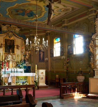 Zdjęcie nr 14: Polichromia ścian kościoła odpowiada podziałom architektonicznym wnętrza wydzielonym przez pilastry. Malowany zielony cokół w jednej czwartej wysokości ścian wyodrębniony jest pasem ornamentu geometrycznego, w nawie w jego polu znajdują się żółte prostokąty z dekoracją geometryczną, w prezbiterium malowana jasnozielona tkanina z dwoma pasami ornamentu roślinnego, medalionami z monogramami Marii i koronami oraz z motywem lilii heraldycznych i rozet. Trzony pilastrów wnętrza bladożółte z malowanymi płycinami dekorowanymi kampanulami, głowice zdobione malowanym kimationem. Na osi pilastrów, w partii fryzu, na tle niebieskich prostokątów uskrzydlone główki anielskie, pomiędzy nimi fryz wypełniony różowo-pomarańczowymi malowanymi płycinami w błękitnym obramieniu o fantazyjnym wykroju, dekorowanymi kampanulami. Belkowanie zamknięte malowanym pasem ornamentu geometrycznego. W polach pomiędzy pilastrami malowane płyciny o fantazyjnym kształcie zbliżonym do prostokąta, ujęte ramą zakończoną kartuszem, ich pola wypełnione są dekoracją geometryczną składającą się z krzyży równoramiennych w glorii i rozet wykonanych techniką patronową. Otwory okienne ujęte są malowanymi, imitującymi profilowanie obramieniami, otwory drzwiowe iluzjonistycznymi portalami z uszakami: portal w nawie zwieńczony jest kartuszem, a portal w prezbiterium zwieńczony jest szczytem zamkniętym fragmentem gzymsu w formie łuku segmentowego nadwieszonego podtrzymywanym przez spływy wolutowe. Pod chórem muzycznym malowane tablice pamiątkowe ujęte ramą, na ścianie północnej z napisem: „Ecclam hanc sub titulo Assumptionis B.V. Mariae a strenuo / milite Wierzbięta in Branice et Ruszcza Haerede pimo in / Wola juxta fines villae Stryjów a D. 1386 fundatam decimis / ex praedio Branice a colonis Stryjów, Wola, cuius sors est Grabie / Szczurów Zymbrzeg et ibidem taberna cum duobus pratis ac lacubus / Orzek et Piotrek ditatam, proper alluviem Vistulae  curatus suus / in hunc locum, qui erat pratum Gruczyn, ecclae dotale transtulit, / Hac tandem post annos 356 collapsa, quam vides, A.R.D. Jacobus Cichoński, parochus Grabiensis a.D. 1742 in loco desolatae  novam erexit. / Consecravit Illmus ac Rmus Michaël Kunicki, Sufraganeus Eppus. / Cracoviensis, Abbas Clarae Tumbae a D. 1749. / Restauravit A.R.D. Josephus Raźny, parochus Grabiensis a.D. 1907. / e colectis parochianorum.”; na ścianie południowej z napisem: „Ku Pamięci! / Dzieci Moje Najmilsze - Ja Prastara Świątynia / Polska dziękuję Wam za serdeczną troskę / o mnie. Oto dzięki Waszym ofiarom Drodzy / Rodzice i Twoim wysiłkom Kochana Młodzieży / w r. 1959 odnowiło się moje oblicze - rozjaśniały /  moje ołtarze, a w r. 1960 zabrzmiał mój nowy / organ na większą chwałę Bożą. Ja Was za to / rodzę na nowo do życia łaski. Ja Was błogosławię / na życie rodzinne. Ja Was prowadzę ku Bogu. Ja / Was także żegnam poraz ostatni, gdy przechodzicie / z tego padołu płaczu do wieczności, aby / Was znowu powitać kiedyś w niebie.”. Na ścianie zachodniej, pod chórem, nad środkowym otworem przejściowym pozostałości dawnego iluzjonistycznego portalu z kartuszem herbowym. Na stropie prezbiterium wydzielone pole o kształcie powtarzającym plan prezbiterium, wewnątrz pole w formie kwadratu o wklęsłych narożach z wpisanym polem o fantazyjnym zarysie zbliżonym do owalu ze sceną Wniebowzięcia Najświętszej Marii Panny. W narożach owalne pola z czterema istotami apokaliptycznymi. Prosta belka tęczowa w kolorze zielonym, o profilowaniach w kolorze niebieskim i różowym, z napisem: „JEZU ZMIŁUJ SIĘ NAD NAMI”. Na stropie nawy prostokątne pole wydzielone grubym bladoróżowym obramieniem z płycinami o nieregularnym kształcie wypełnionymi kratką regencyjną i rozetami alternowanymi medalionami z rozetami, naroża dekorowane są wstęgą regencyjną i akantem. Wewnątrz pole o fantazyjnym wykroju zbliżonym do owalu ze sceną Koronacji Najświętszej Marii Panny, flankowane przez dwie malowane błękitne płyciny o nieregularnym kształcie wypełnione rozetkami. W narożach, w ozdobnych kartuszach herby Pogoni Litewskiej i Orła Białego.
